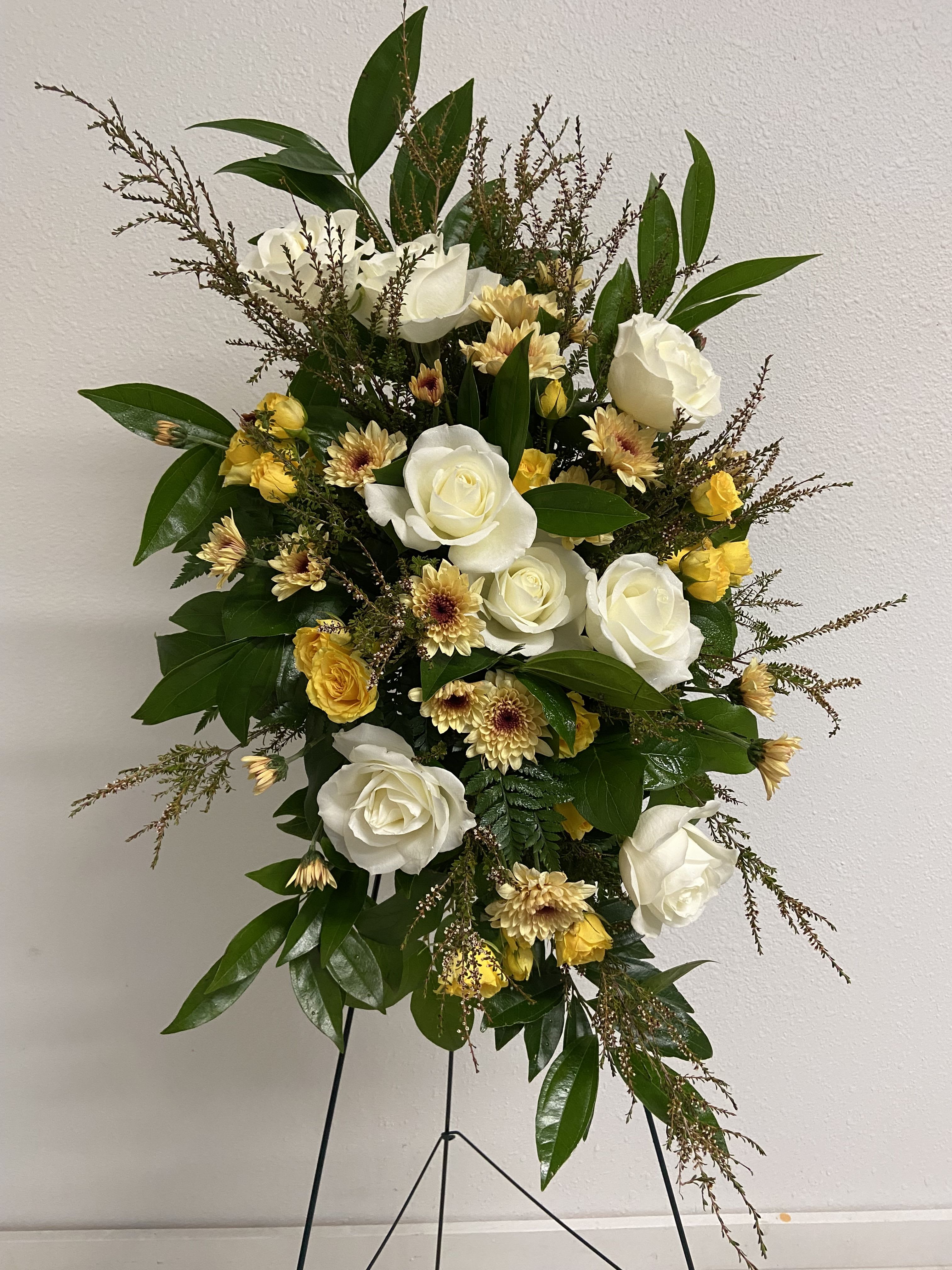 Standing spray of white roses and yellow flowers on a metal easel