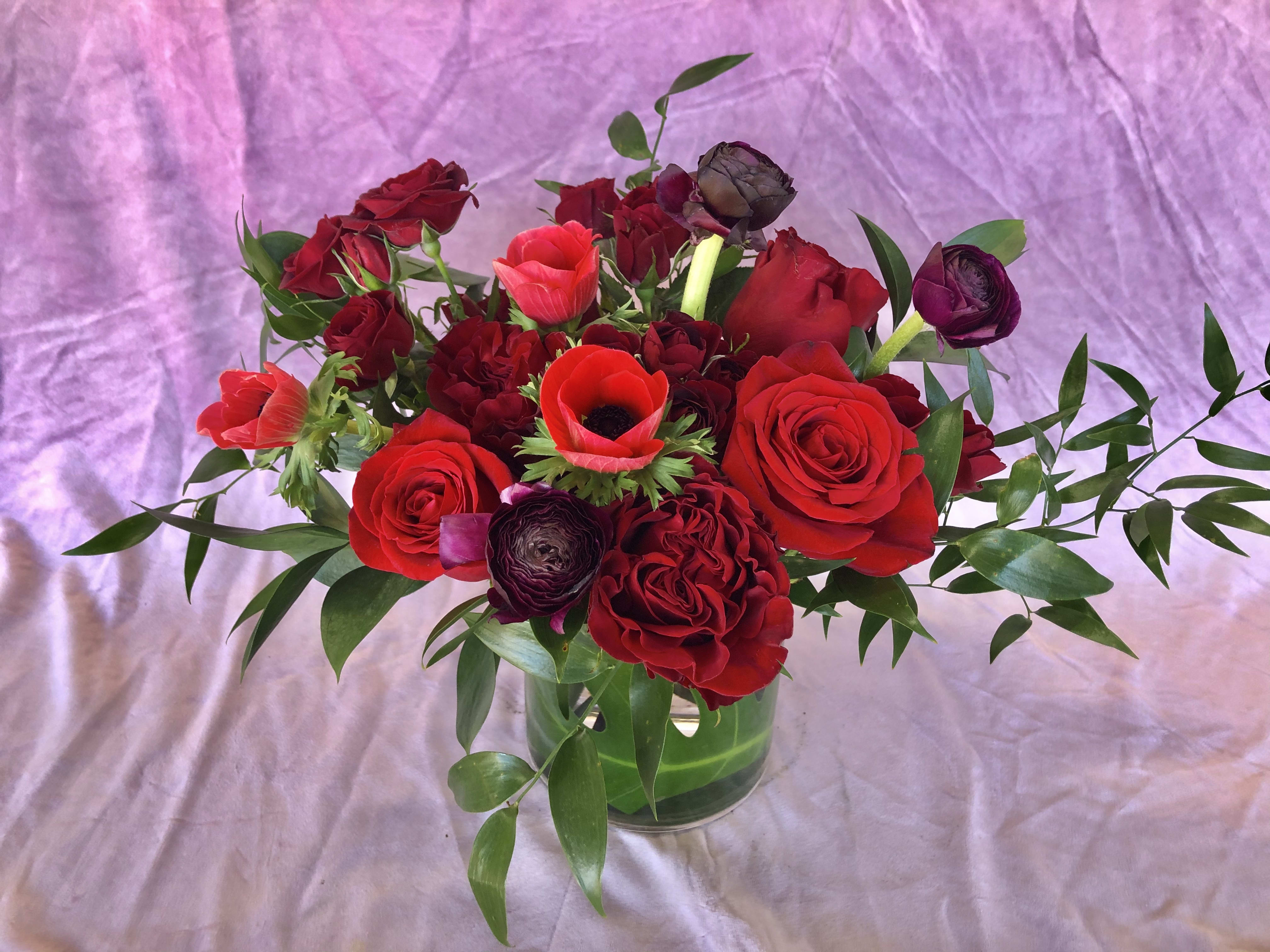 Red roses and dark ranunculus in a glass vase