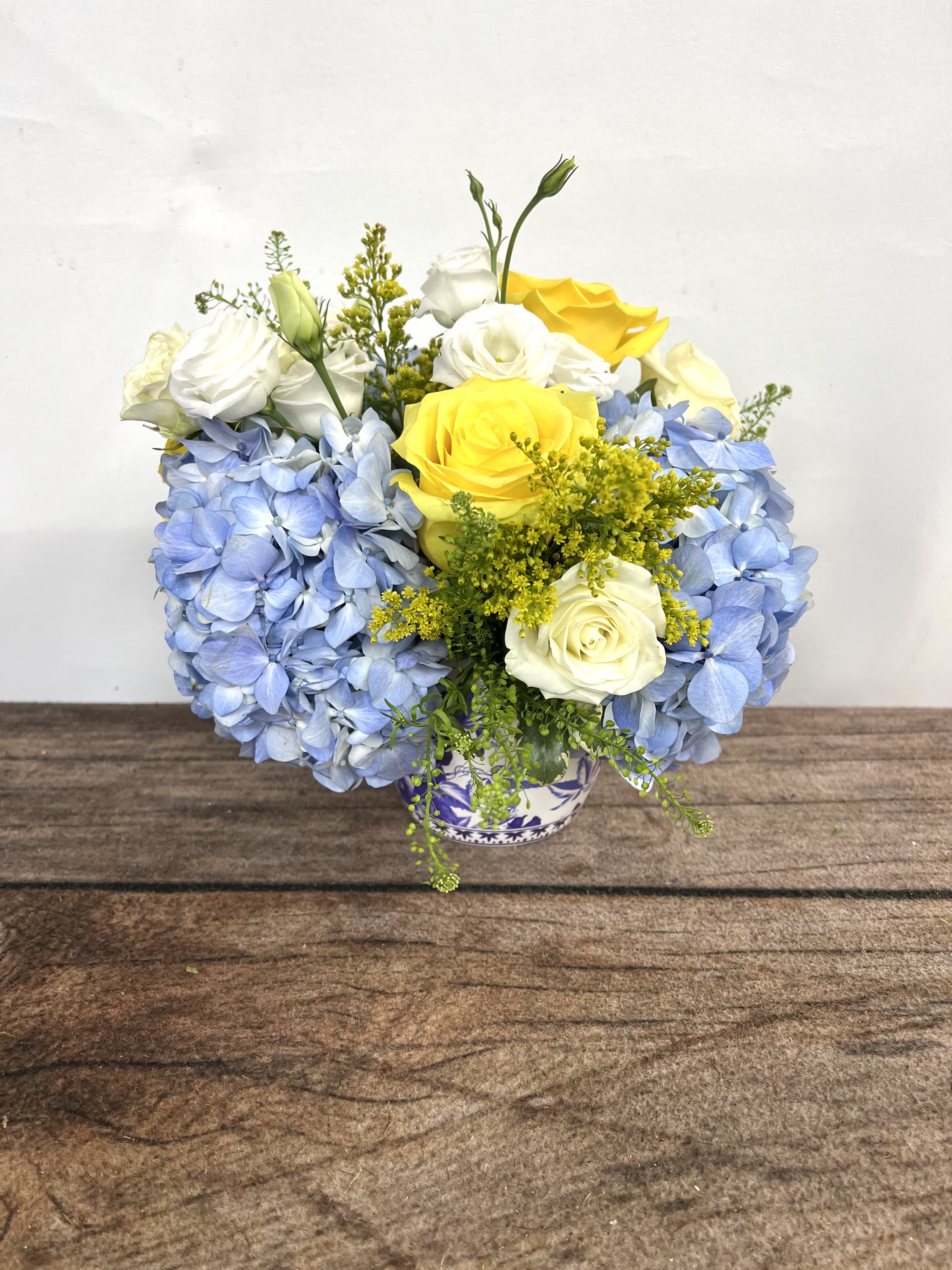 Blue hydrangeas with yellow and white roses in a small vase