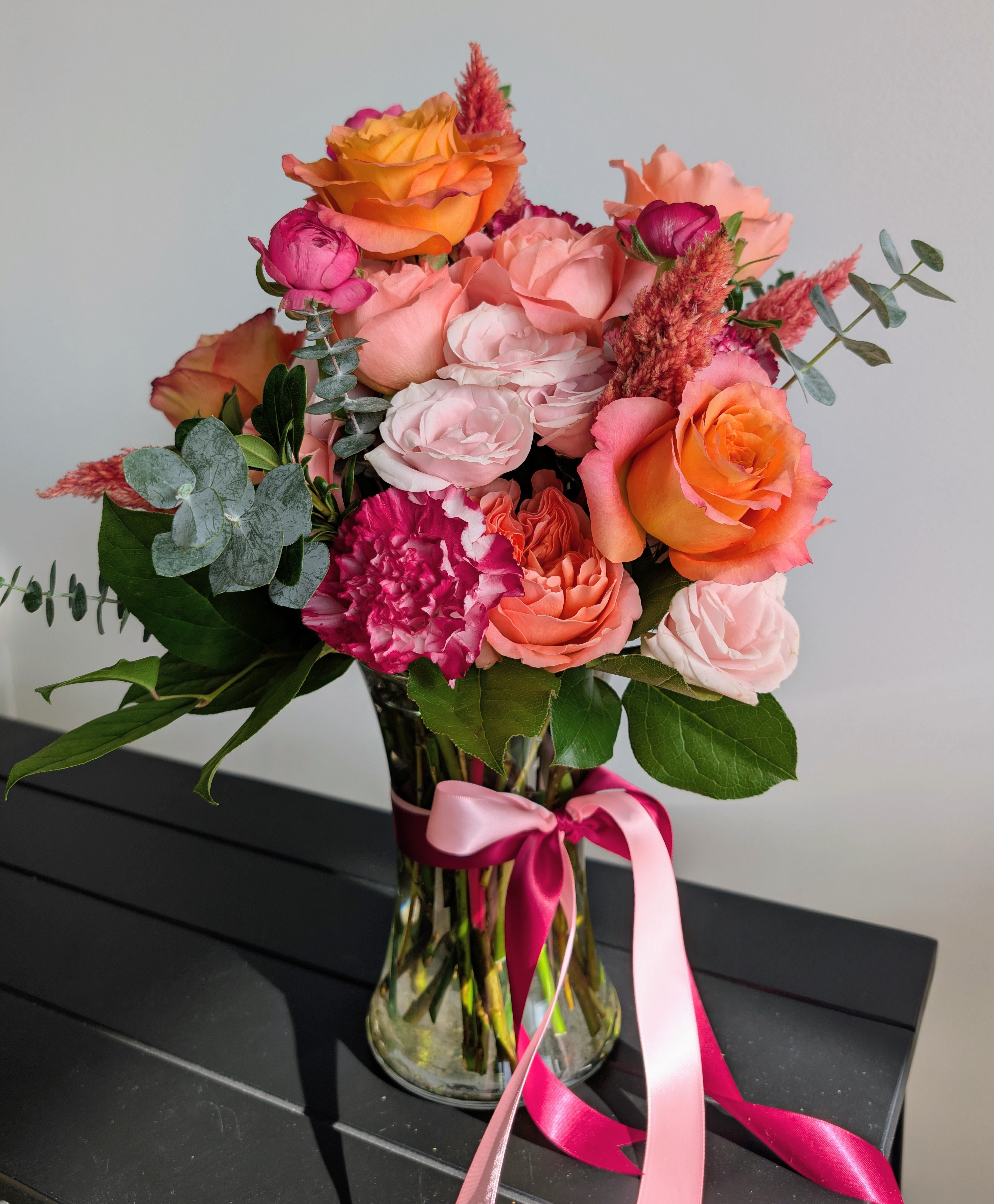 Bouquet of pink and orange roses in a glass vase with a pink ribbon