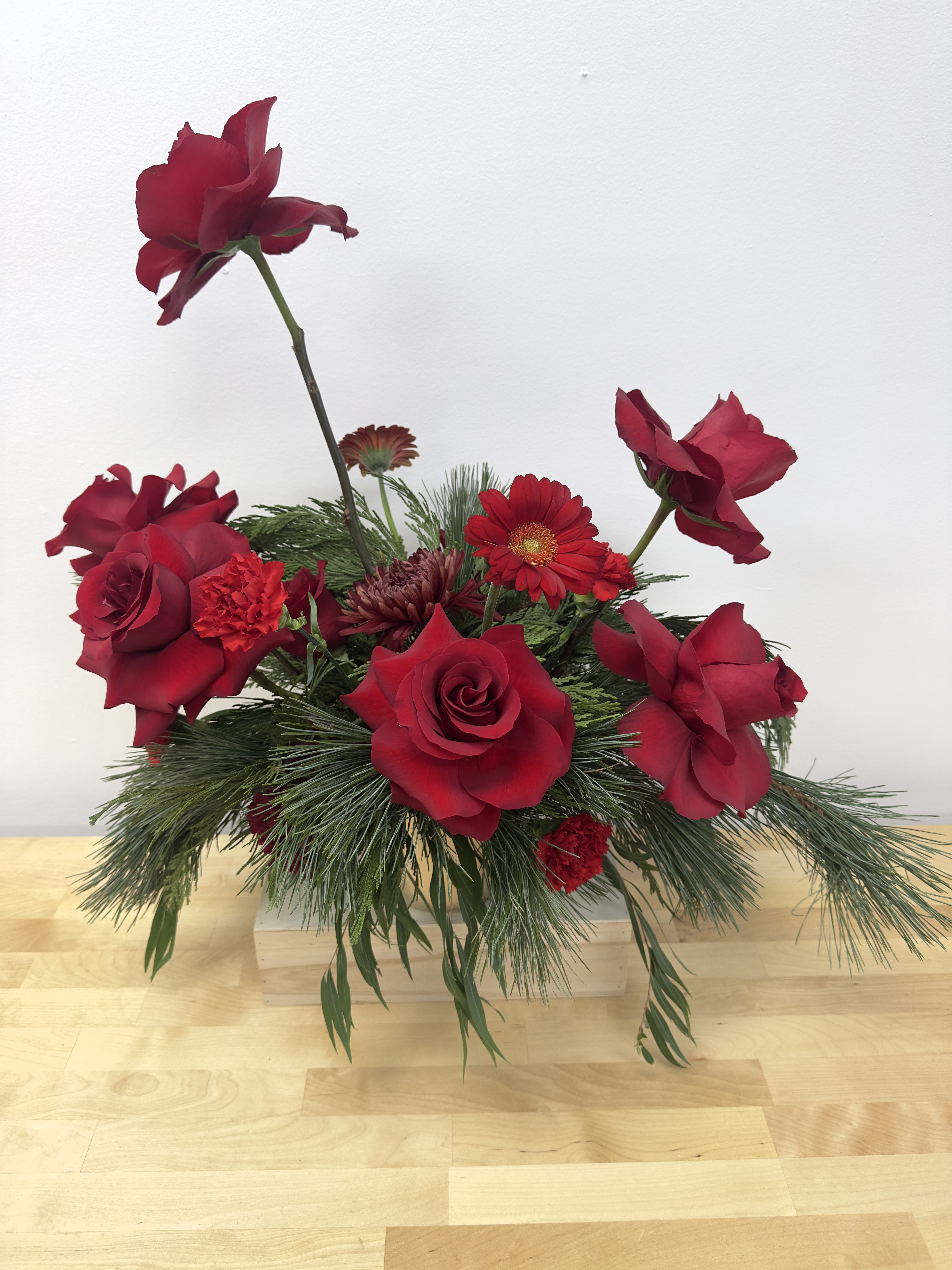Red roses and mixed red flowers in a low arrangement with pine greenery