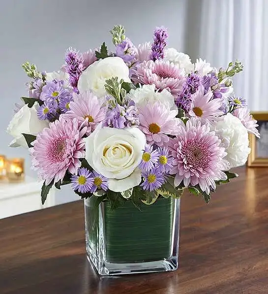 Healing Tears   Lavender &amp; White  - Sometimes in soothing the tears of another, we soothe our own sadness, as well. Our sympathy arrangement of calming lavender stock, daisy poms, white roses and carnations, expertly gathered together in a clear glass cube lined with Ti leaf ribbon, is a graceful gesture of comfort and healing.