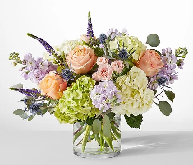 Mixed bouquet of peach roses, hydrangeas, and purple flowers in a glass vase