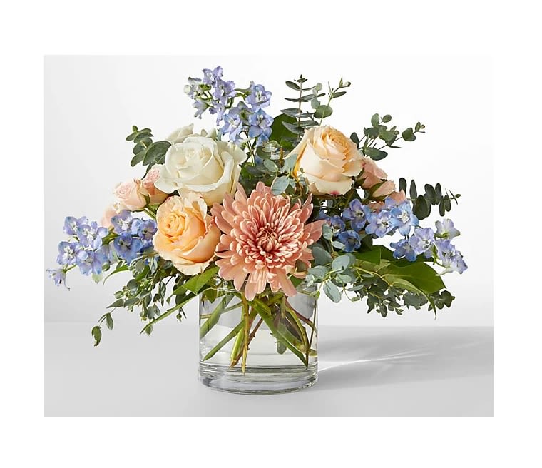 Mixed bouquet of roses, a pink chrysanthemum, and blue flowers in a glass vase
