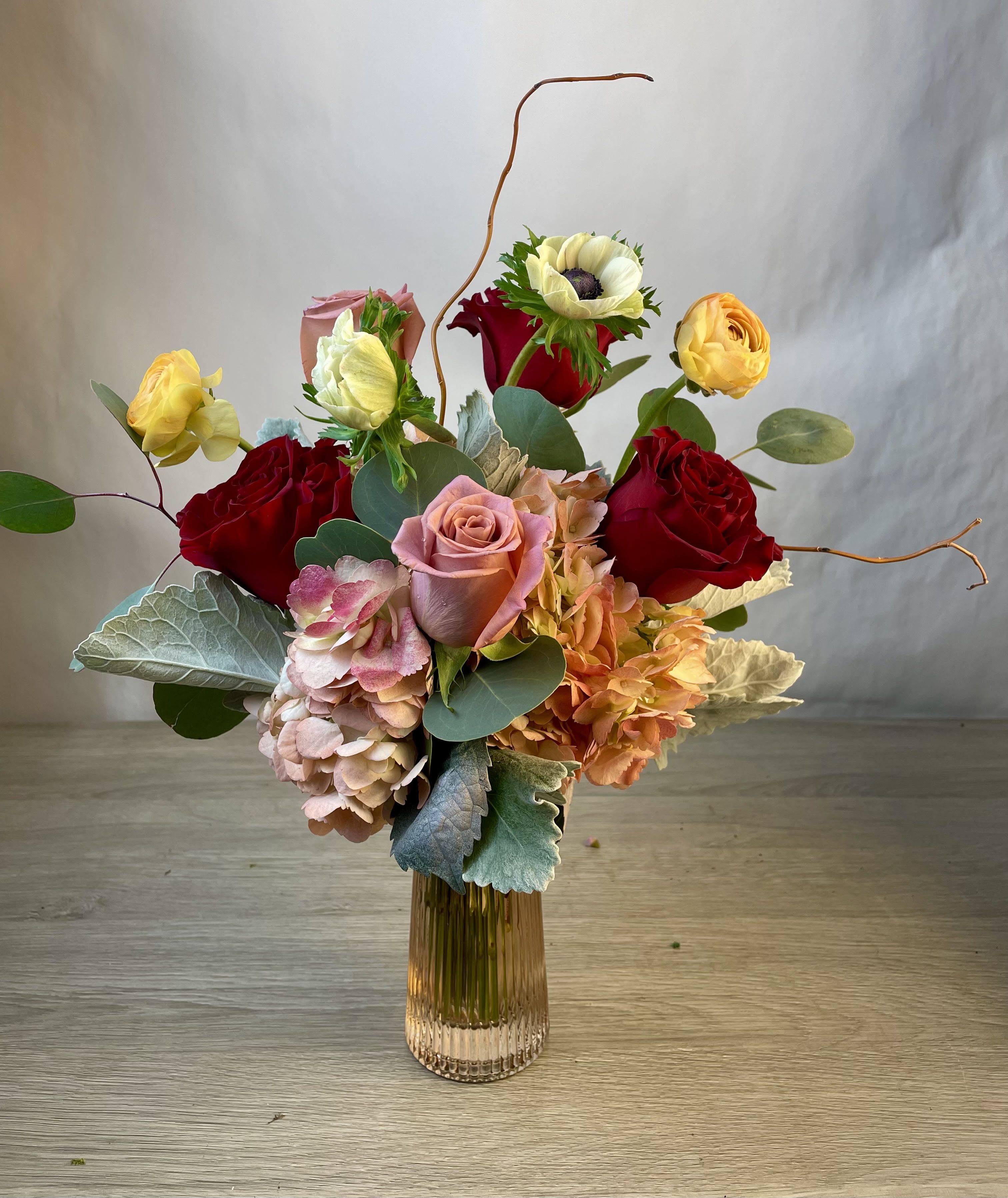 Mixed bouquet of roses, hydrangeas, and anemones in a glass vase