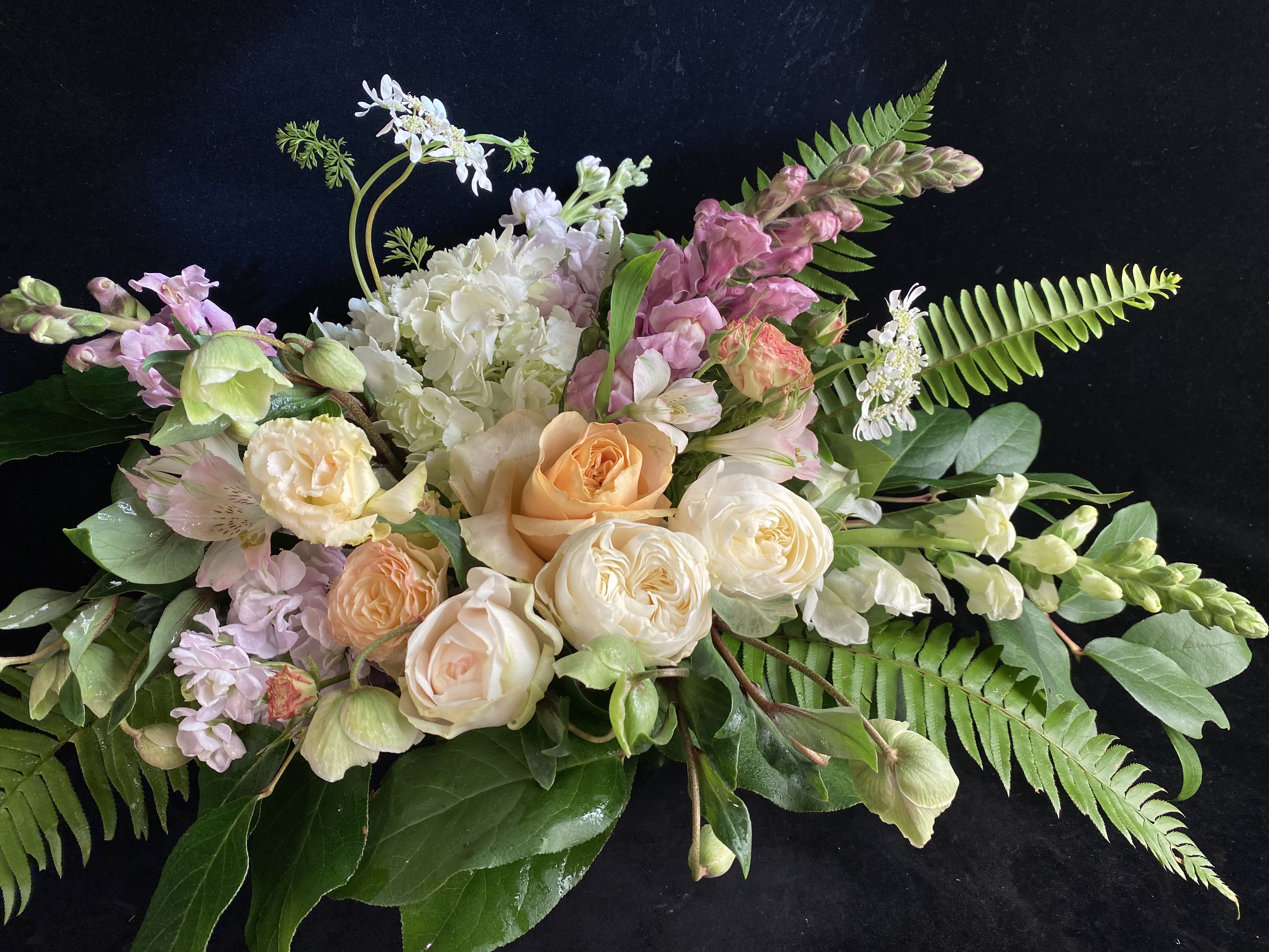 Pastel floral arrangement with roses, hydrangea, and snapdragons on a dark background