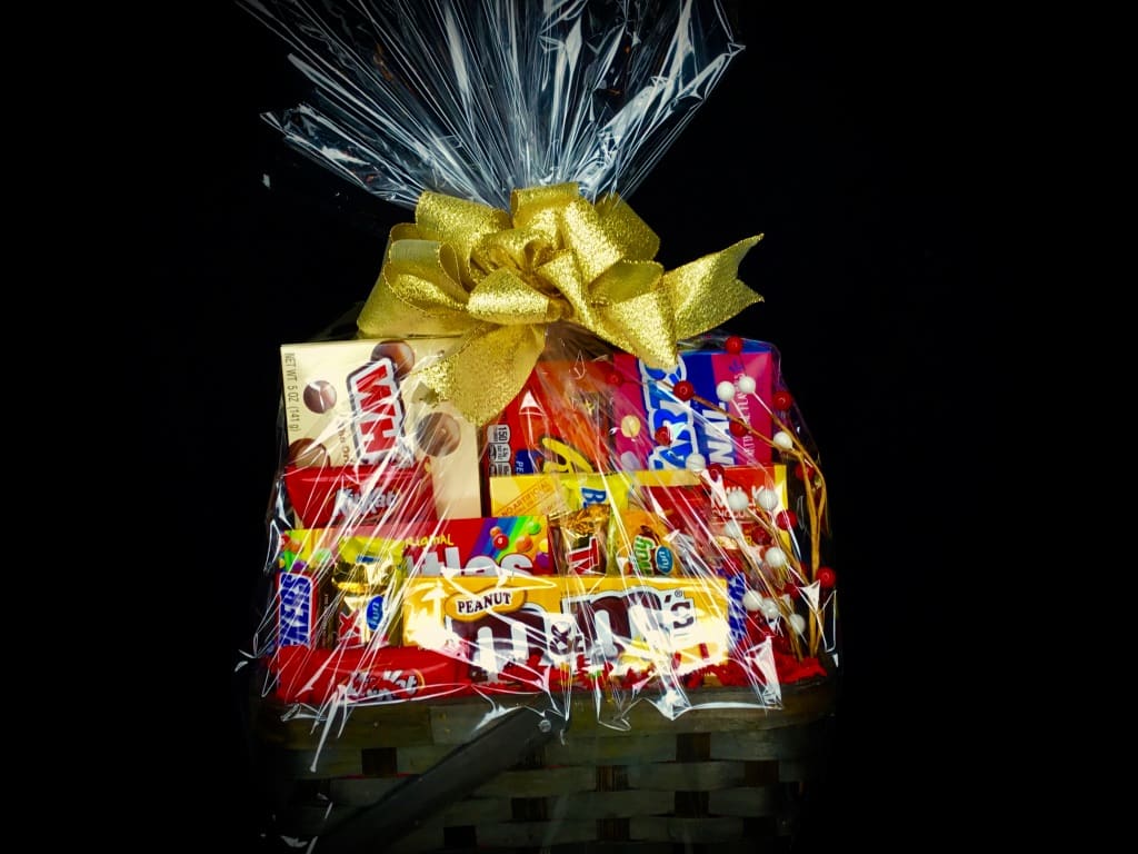 Basket of assorted candy bars wrapped in clear cellophane with a gold bow