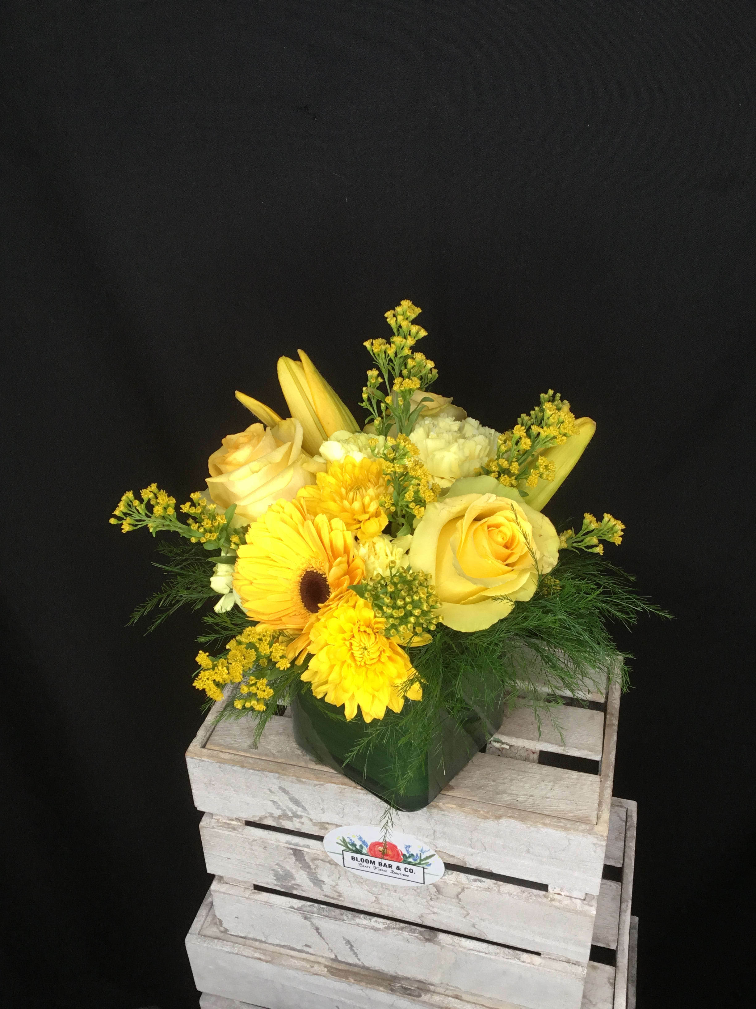 Yellow floral arrangement in a green vase with roses and daisies