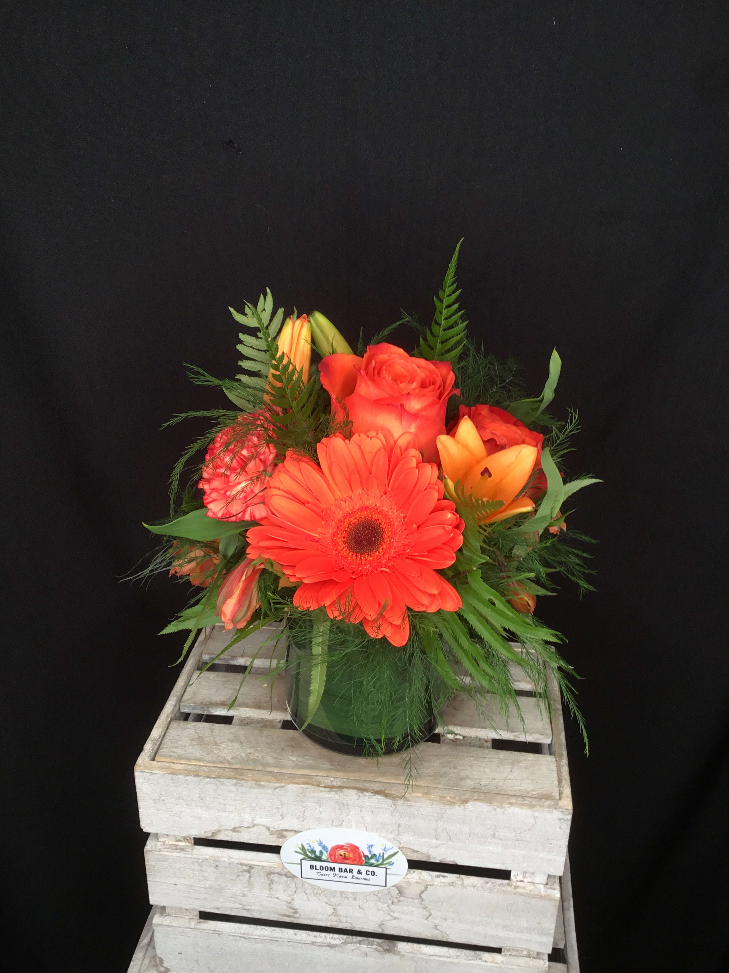 Orange gerbera daisy and roses in a glass vase