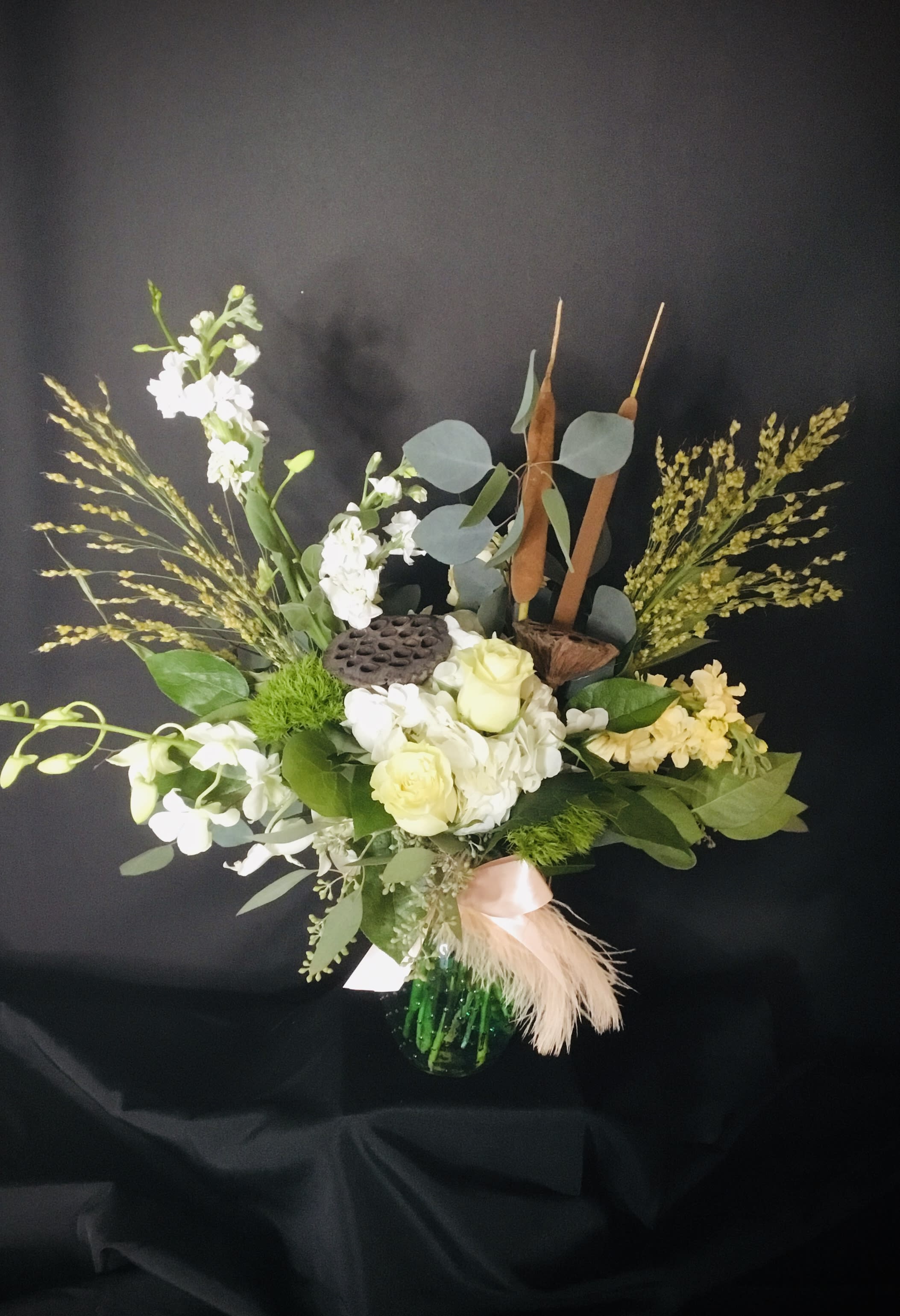 Mixed floral arrangement in a green vase with white blooms and tall seed heads