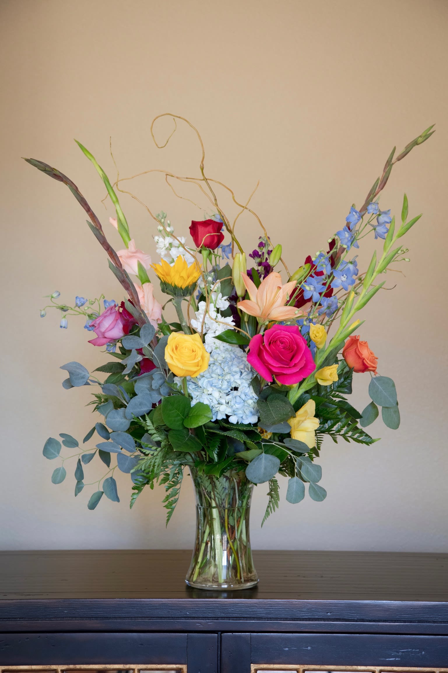 Mixed bouquet of roses, lilies, hydrangea, and blue delphinium in a glass vase