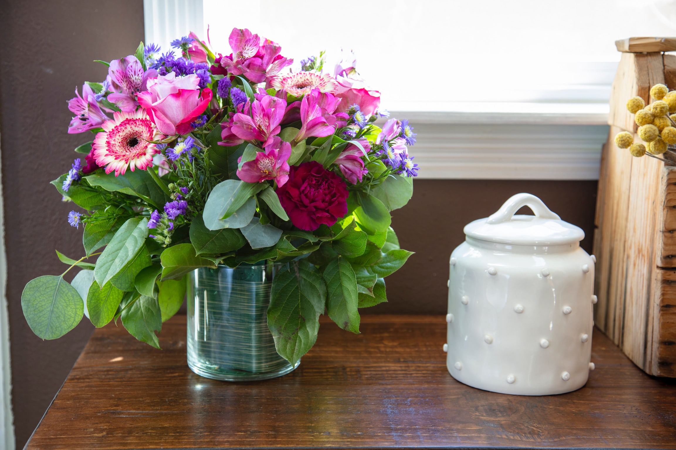 Pink and purple mixed bouquet in a glass vase beside a white ceramic jar
