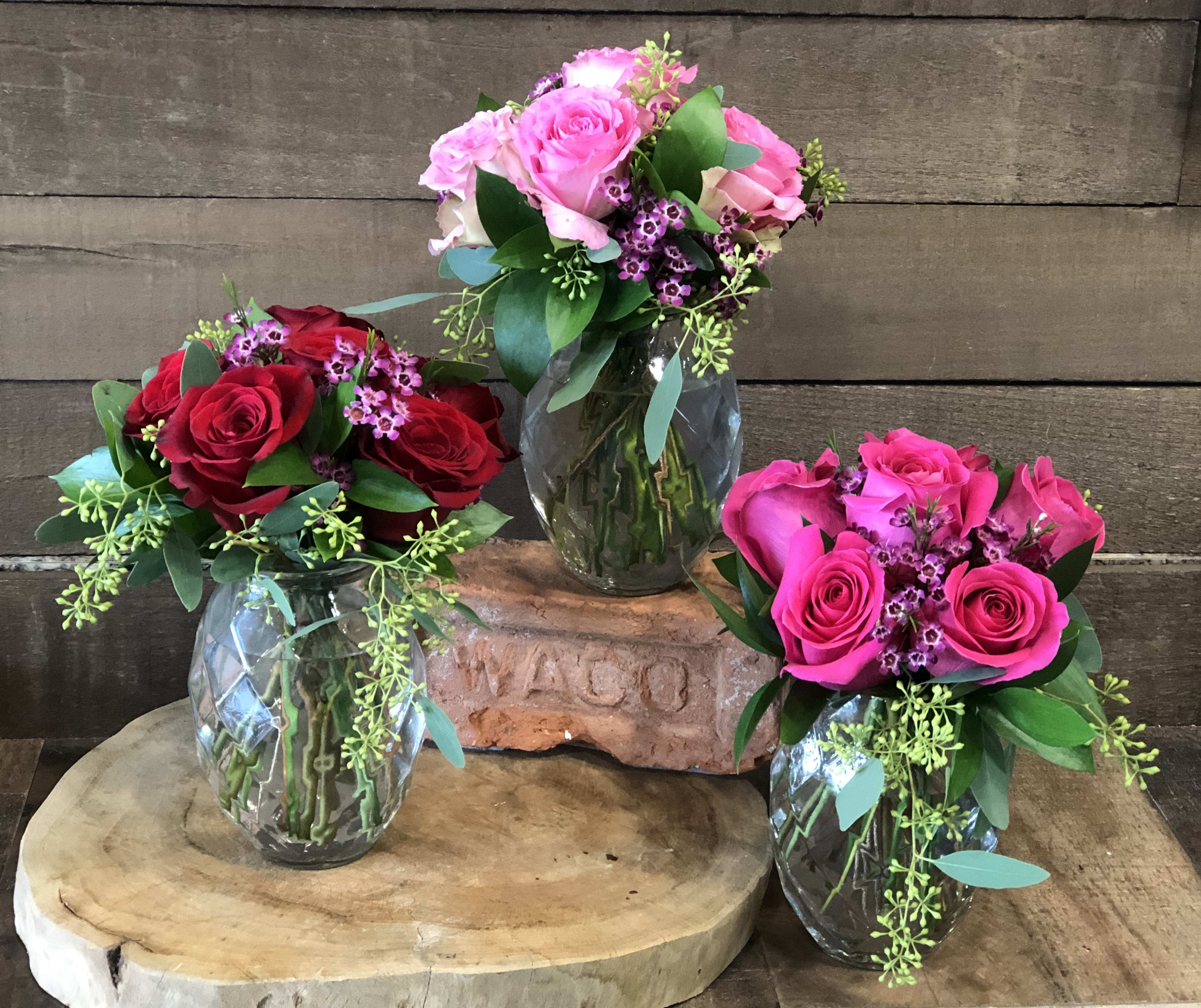 Three rose bouquets in glass vases on wooden stands