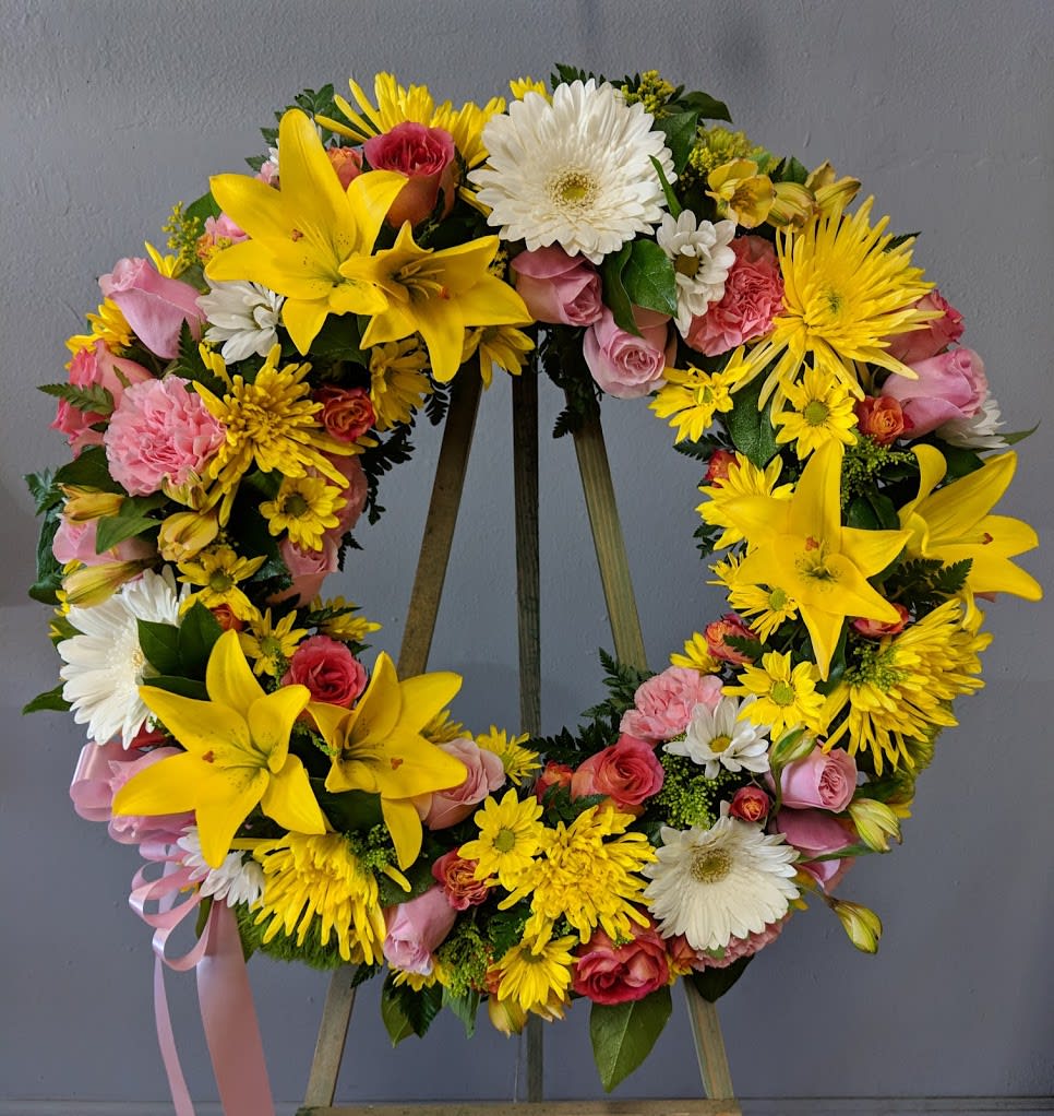 Circular floral wreath with yellow lilies, pink roses, and white daisies on an easel