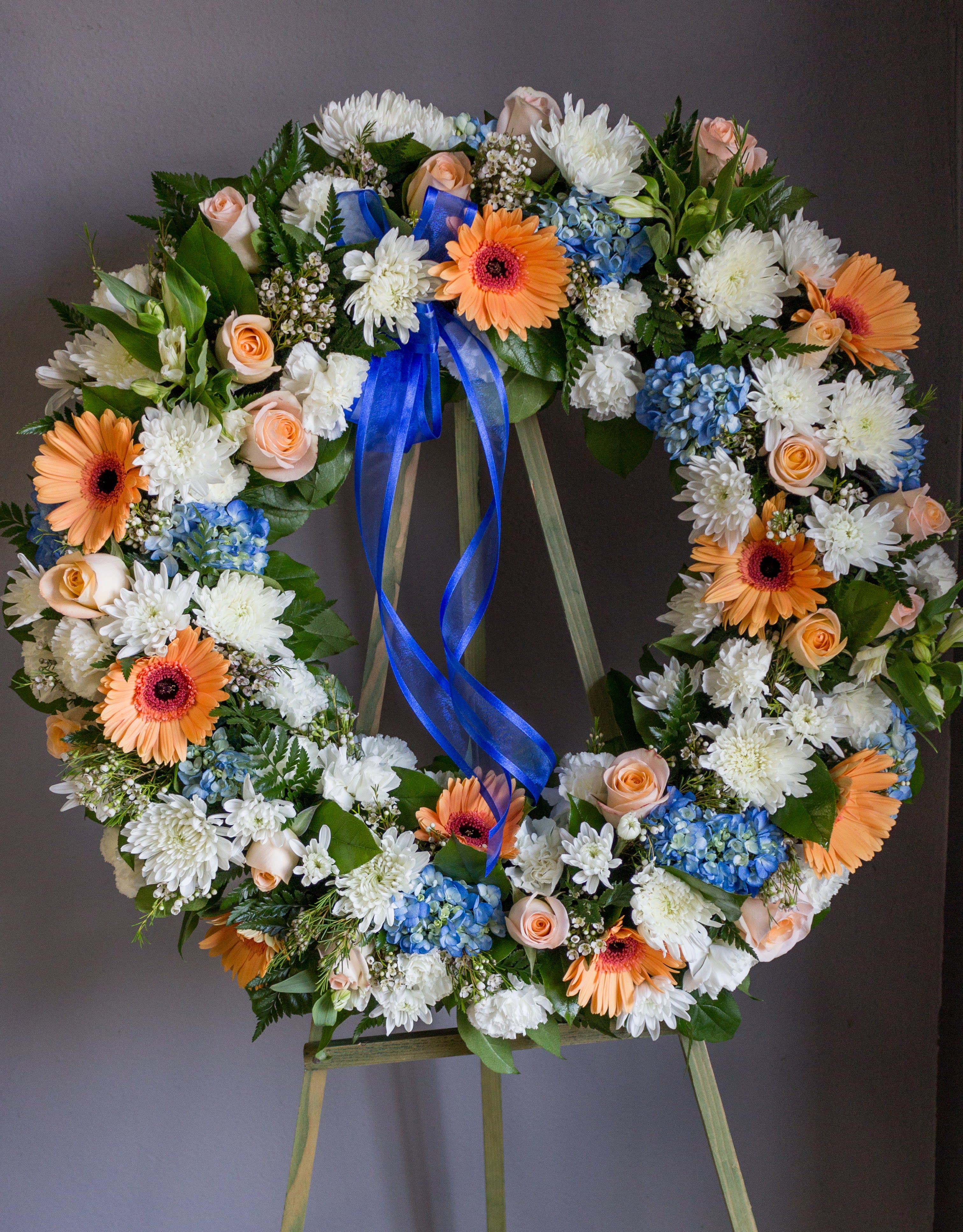 Floral wreath with white, peach, blue, and orange blooms on an easel