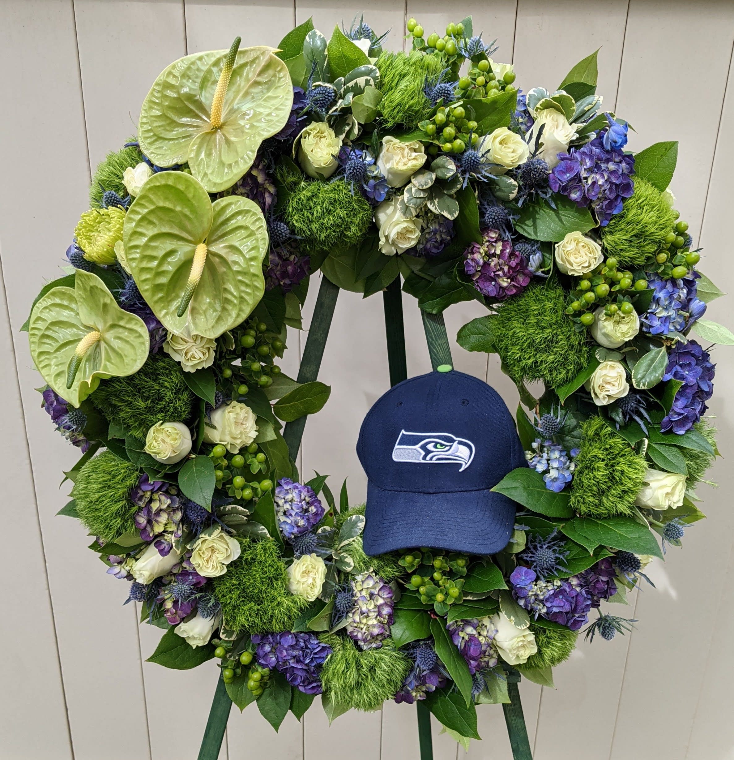 Large floral wreath with white roses, purple hydrangeas, and green anthuriums around a blue cap