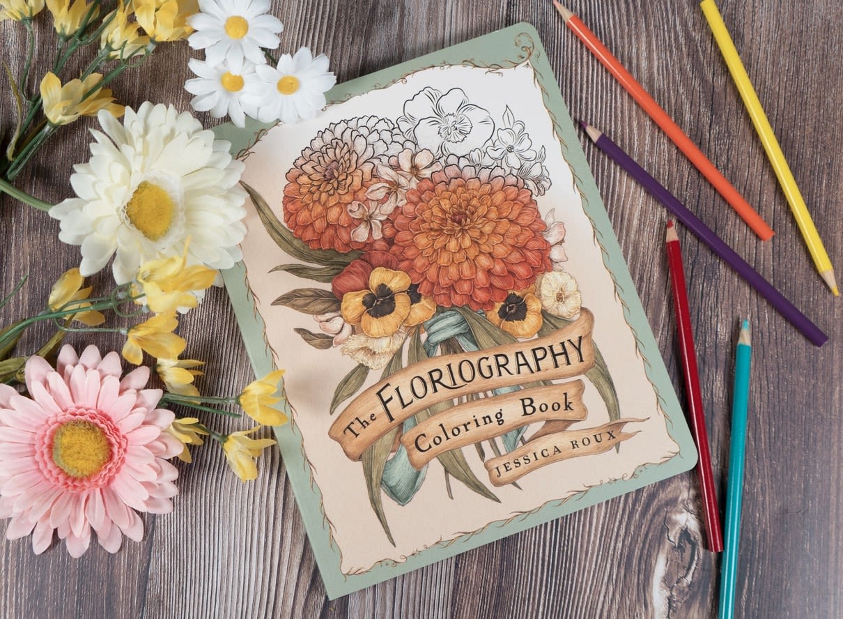 Coloring book with paper flowers and colored pencils on a wood surface