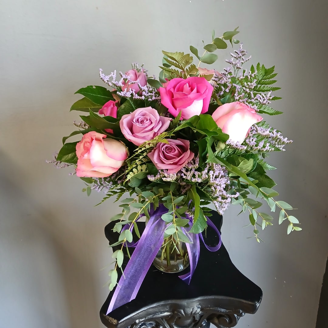 Pink and lavender roses arranged in a glass vase with a purple ribbon.