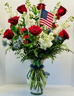 Red roses and white flowers in a clear vase with a small American flag
