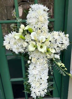 Cross with callas - A dignified white floral cross that speaks for you when words fall short - designed for sympathy and funeral services or to say "I'm sorry" with sincere grace. This 36" arrangement presents a soft, cloud-like field of small white chrysanthemums as its base, the all-white palette and classical cross shape creating a reverent, peaceful focal tribute for a graveside, memorial table, or church sanctuary.  A diagonal band of larger white calla lilies and spray roses creates a gentle runway of texture and contrast across the center, while extra mini callas and abundant spray roses add fullness and depth. The mix of chrysanthemum button blooms with the smooth, sculptural callas gives the piece both visual calm and sculpted elegance; green foliage peeks through only subtly to enhance the fresh white tones.  Appropriate for sympathy, a funeral, or when you want to let someone know they're in your thoughts, this cross is made to be a lasting statement of comfort and respect. Sized at approximately 36" for a commanding presence, it arrives ready to display at services; minimal care is needed beyond keeping it cool and away from direct sun until placement.