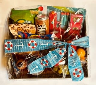 Nautical or Nice - Bright and playful, this gift basket leans into a nautical theme with a wide blue ribbon printed with anchors and life preservers-perfect as a casual birthday gift, thank-you, or just-because surprise for someone who loves seaside charm. The clear cellophane wrap keeps the colorful snack packages and soda can visible, so the recipient immediately feels delighted by the cheerful presentation and thoughtful, ready-to-enjoy contents.  Arranged in a shallow basket, the mix of red, blue, green and yellow packaging creates an upbeat, sunny palette that reads as both fun and familiar. Included hard goods-assorted packaged snacks and a soda can-are neatly secured and finished with a decorative ribbon so the basket arrives gift-ready. Sized for easy pickup or delivery, it's an excellent pick when you want to send a lighthearted treat that shows you're thinking of them without fuss.