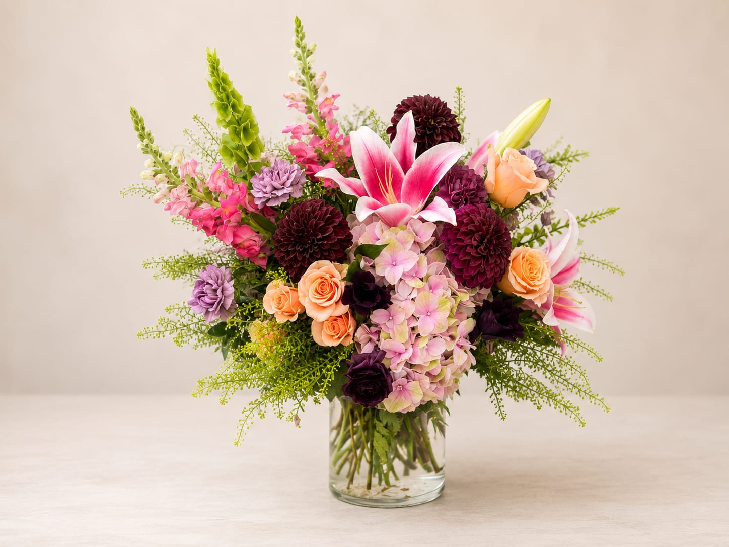 Summer Luxury - A lush, rounded mixed bouquet that reads like a summer celebration-this flower arrangement is a premium flower arrangement perfect for birthdays, thank-you gifts, or a bright spring surprise. The generous mix of pink lilies, peach roses, lavender hydrangea, and rich  dahlias creates an immediate visual lift; tall green snapdragon spikes add vertical movement so the person you're sending it to feels seen and celebrated.  Ideal for marking birthdays, thanking a friend, or brightening a mantel during spring and summer, this composition sends a message of warmth and joy. As a limited-edition weekly drop, availability is exclusive-order soon to ensure delivery. For best enjoyment, place in fresh water, keep out of direct heat, and trim stems slightly if needed to extend vase life.