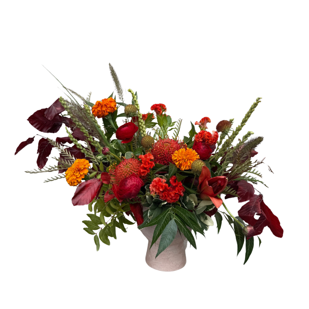Mixed red and orange floral arrangement in a light vase
