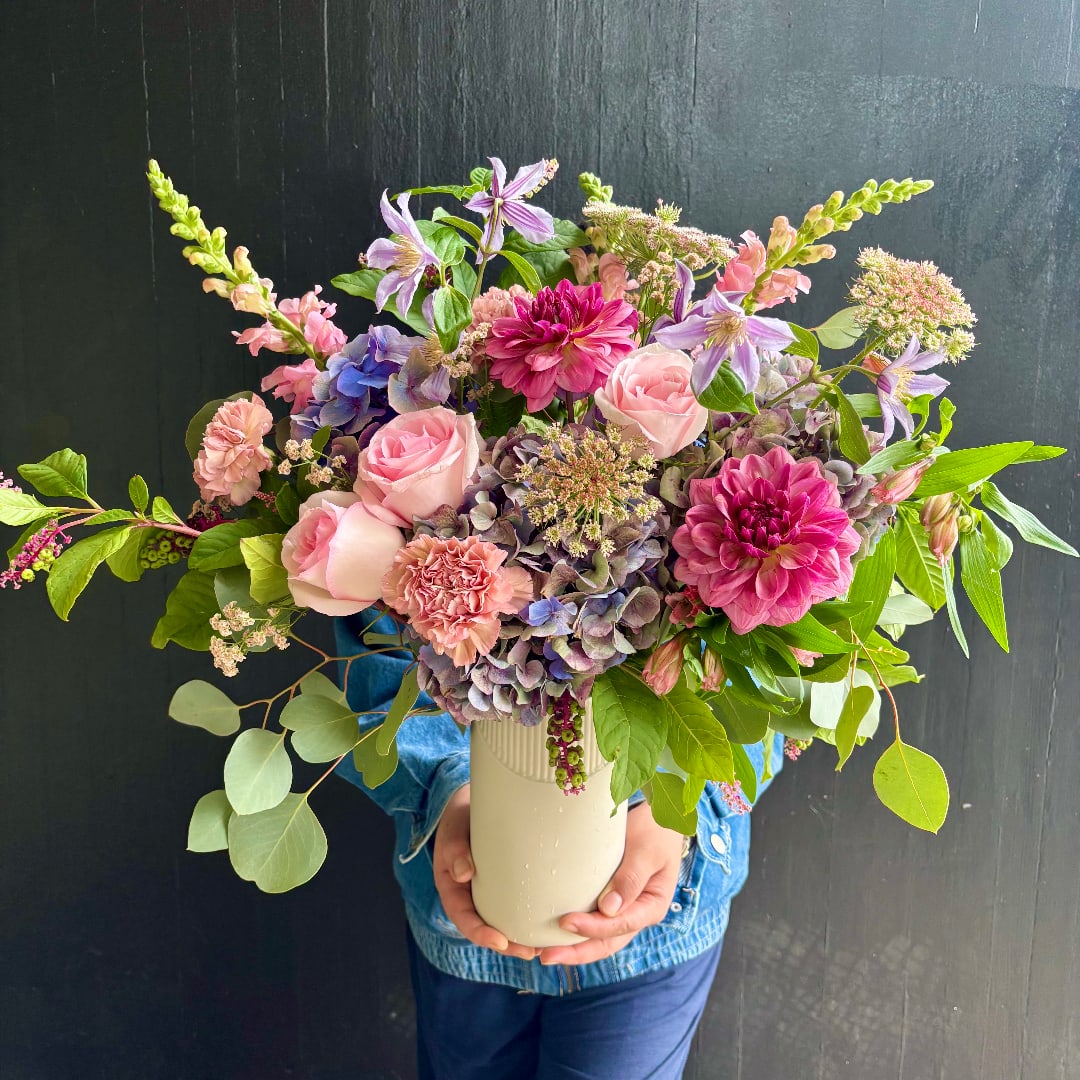 Mixed bouquet of pink, purple, and peach flowers in a cream vase