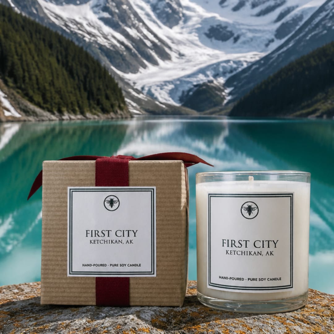A boxed candle beside a glass jar candle on a rocky surface.