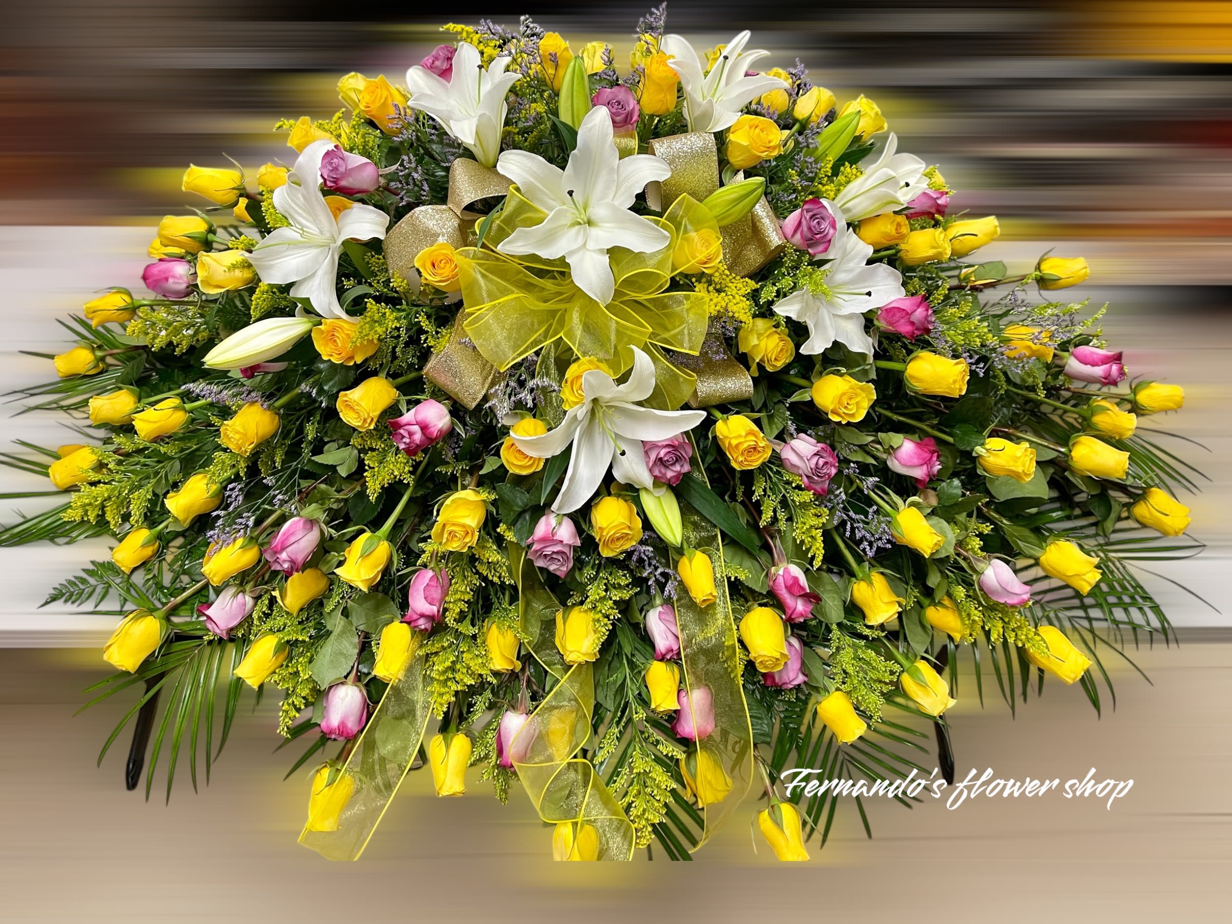 Large casket spray of yellow and pink roses with white lilies and yellow ribbon bows.