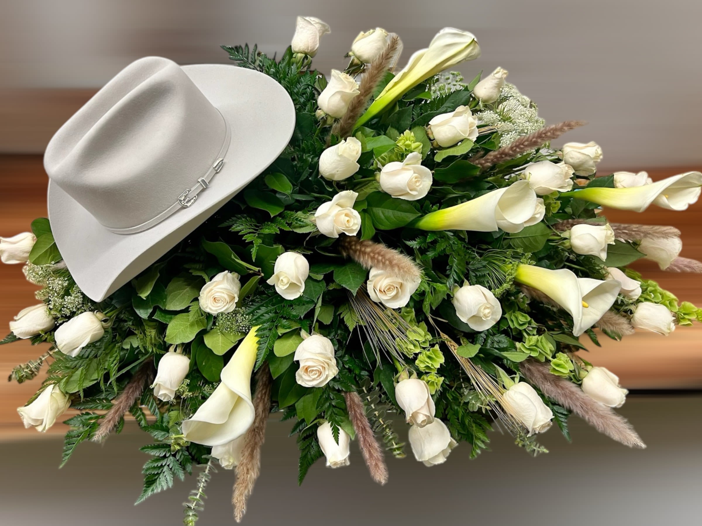 Sympathy spray of white roses and calla lilies with a light cowboy hat on top