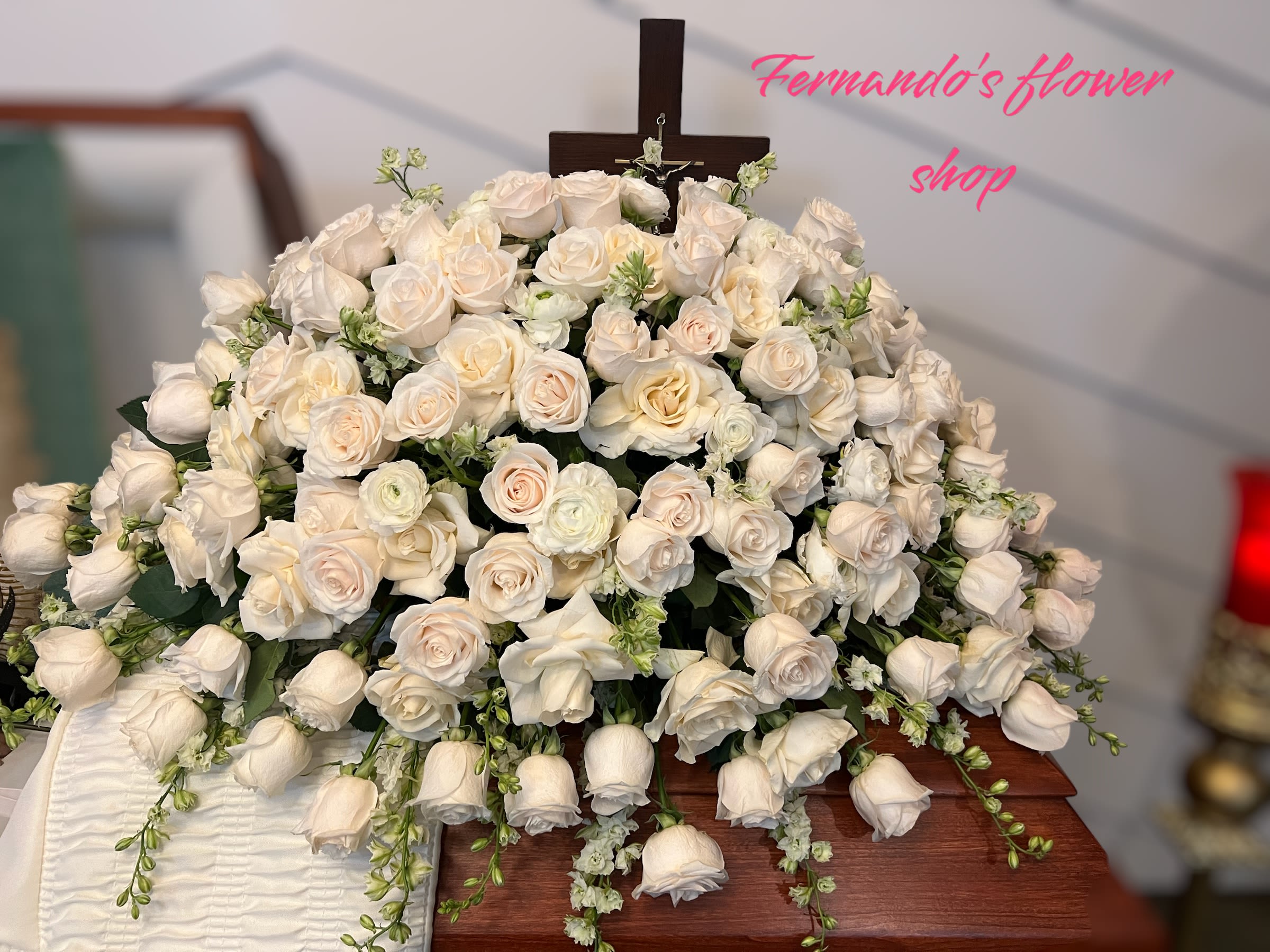 Large spray of ivory roses on a wooden casket with a cross at the back