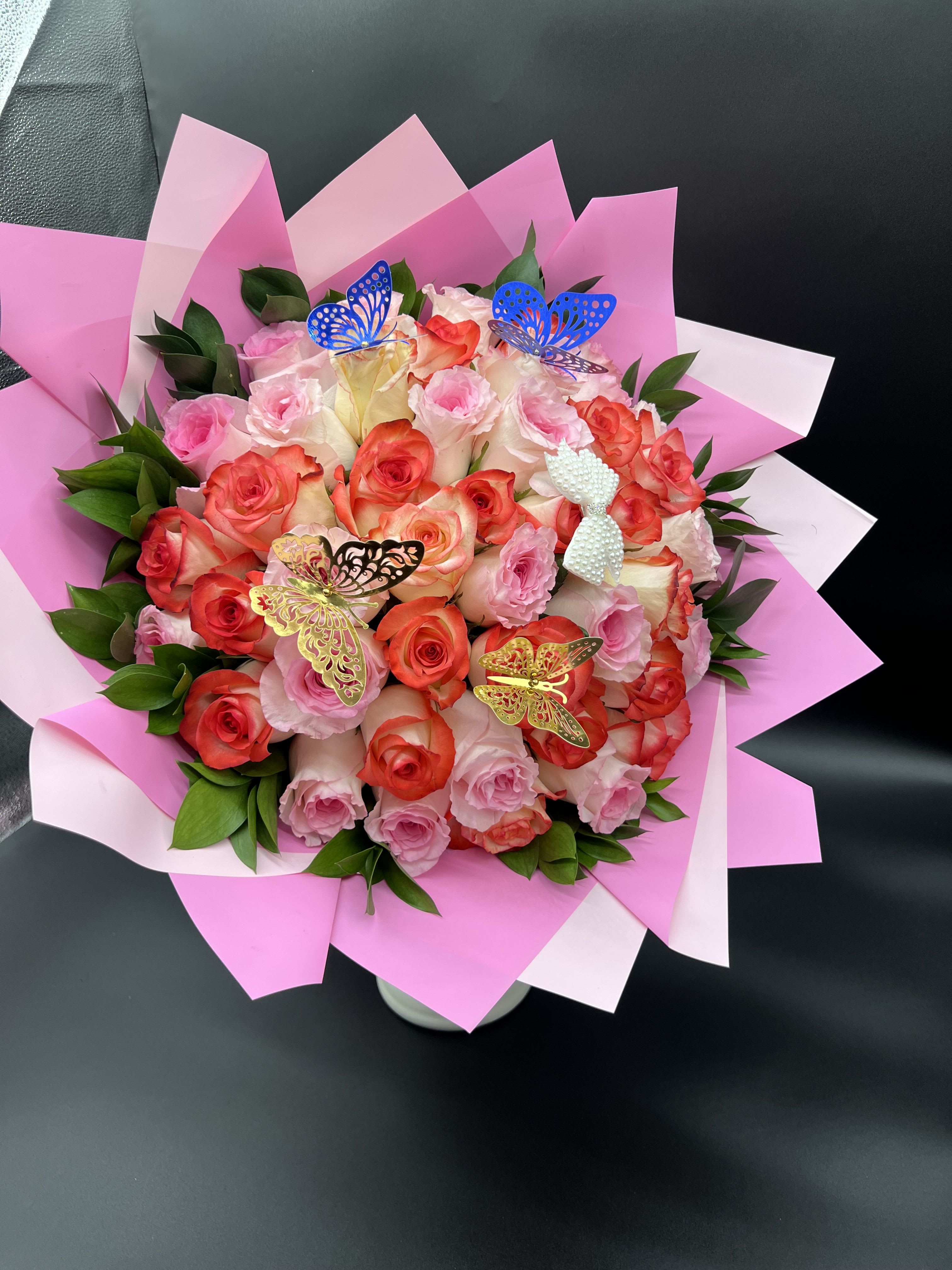 Round bouquet of pink and coral roses with butterfly accents wrapped in pink paper