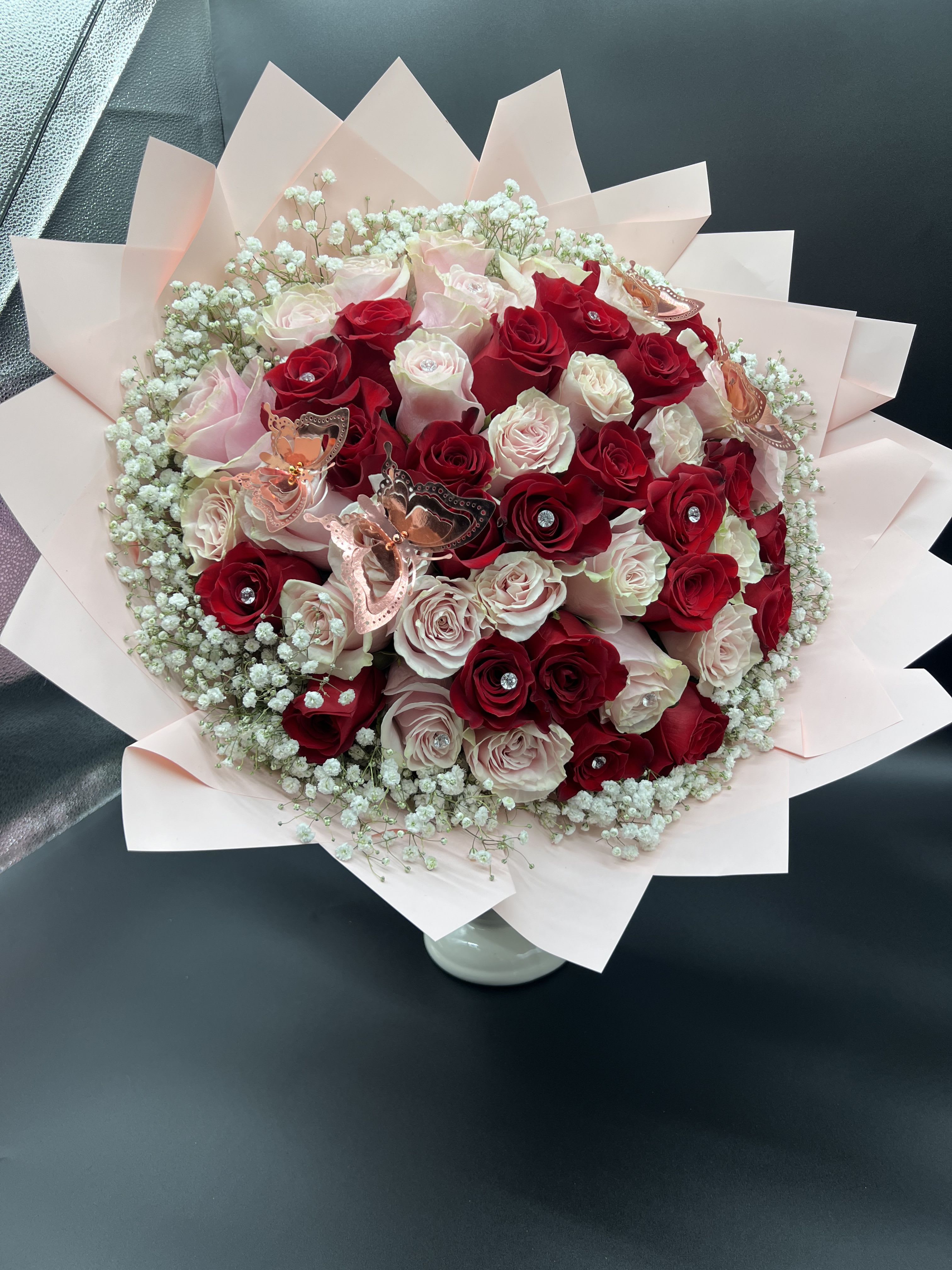 Round bouquet of red and blush roses with baby's breath in pink wrapping paper.