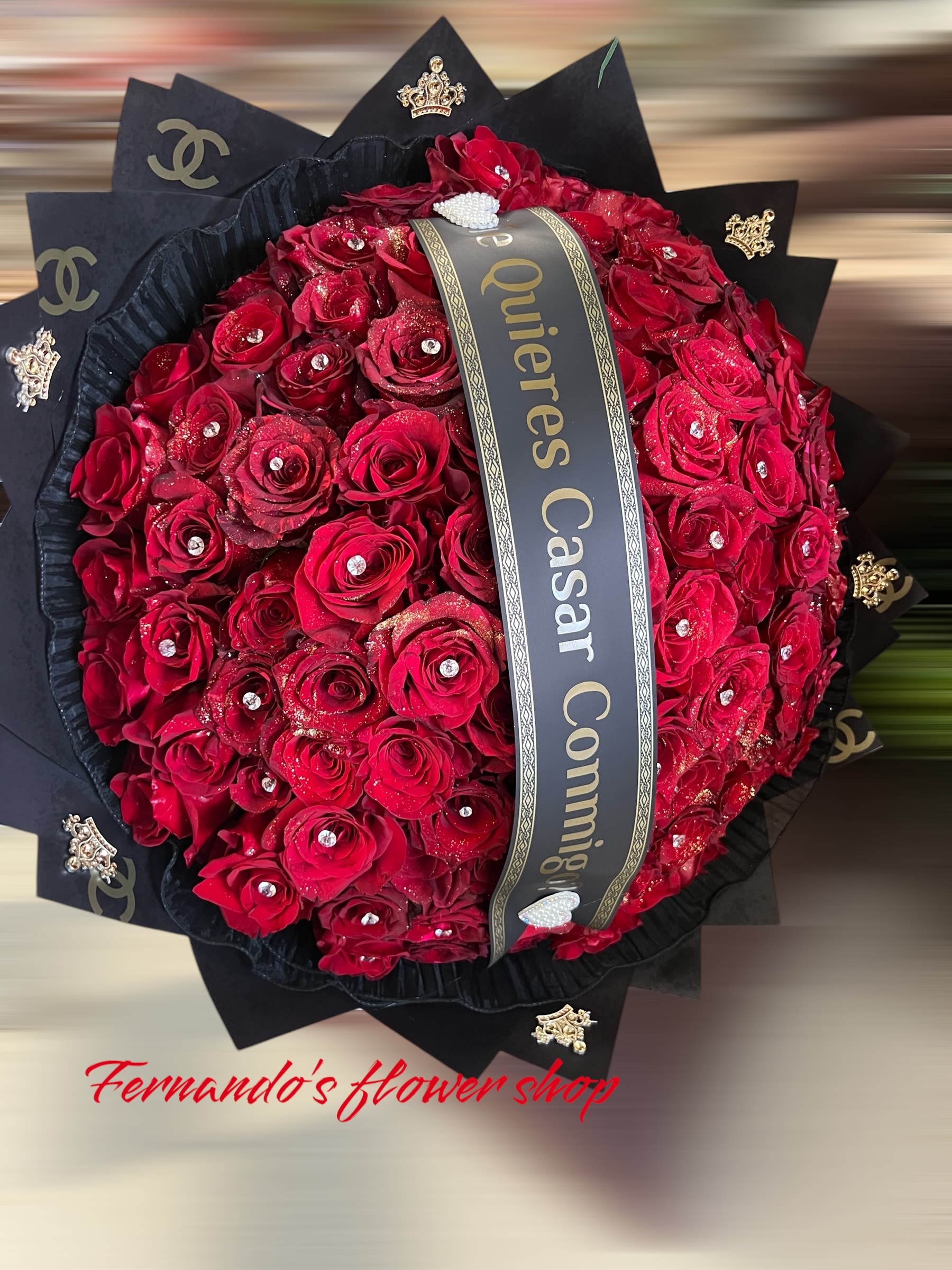 Large round bouquet of red roses with rhinestones, black wrapping, and a printed proposal ribbon.