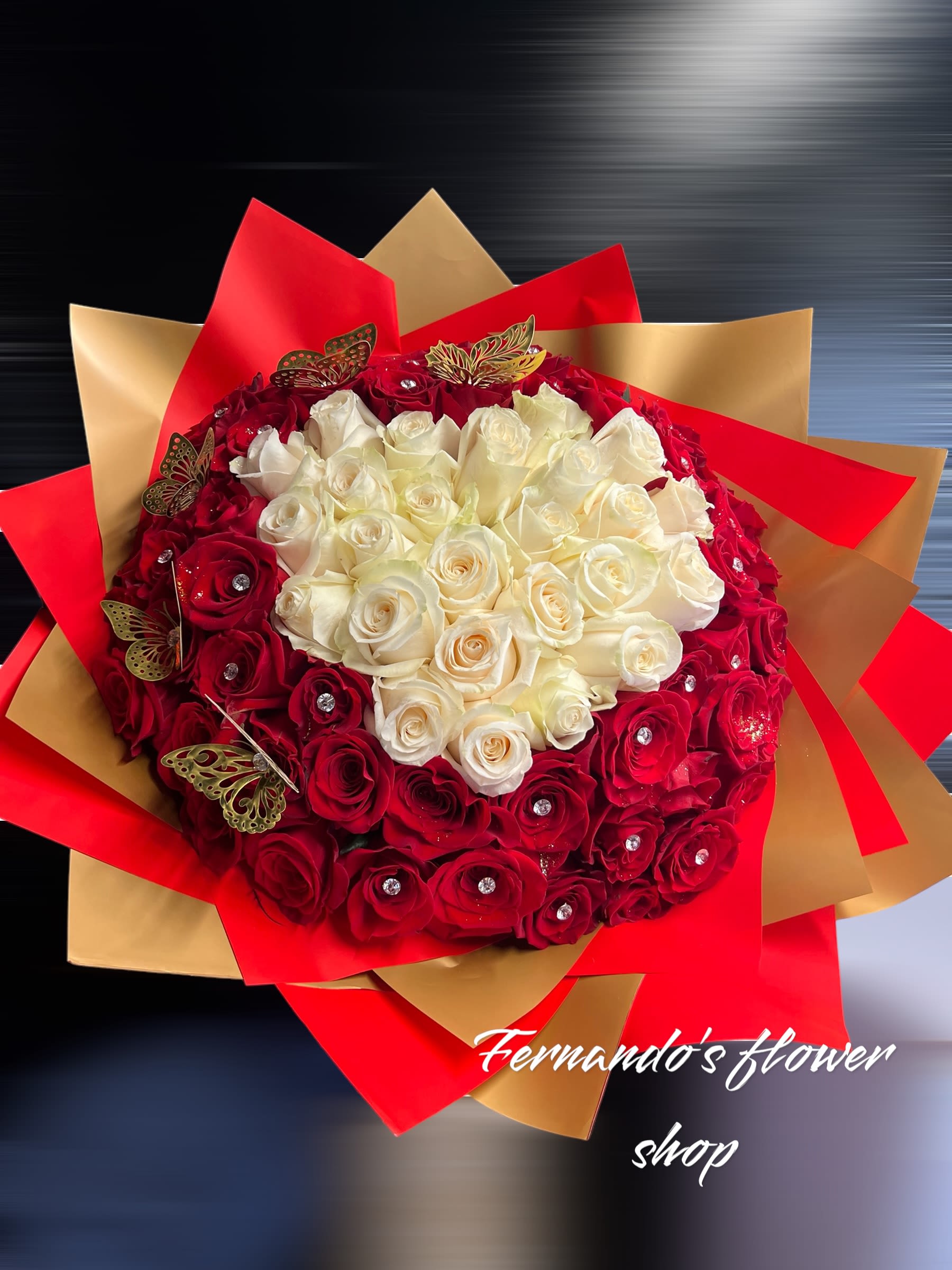 Large round bouquet of red and white roses with jeweled centers, wrapped in red and gold paper