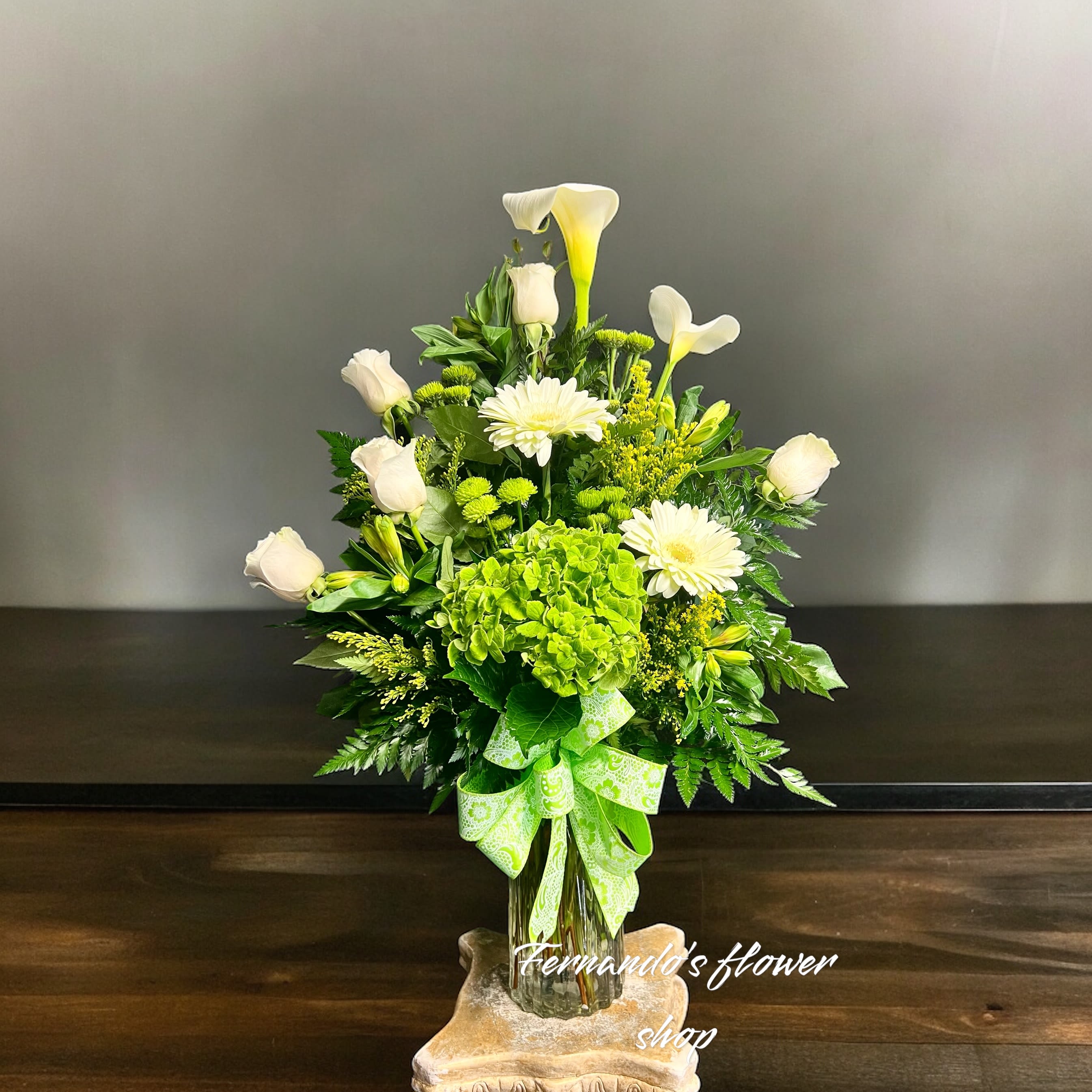 Tall white and green flower arrangement with roses, calla lilies, and hydrangea in a glass vase