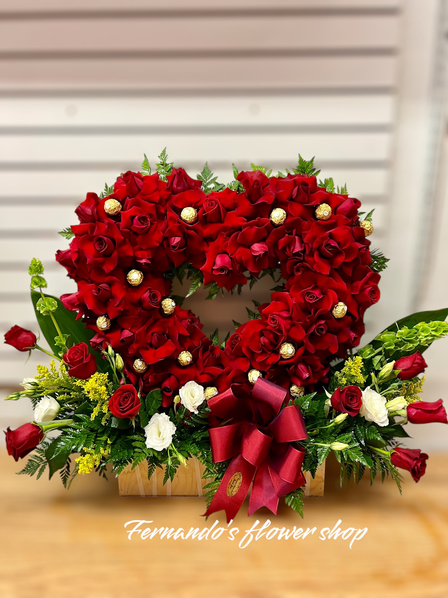 Heart-shaped arrangement of red roses with chocolates and base of red and white roses in a wooden box
