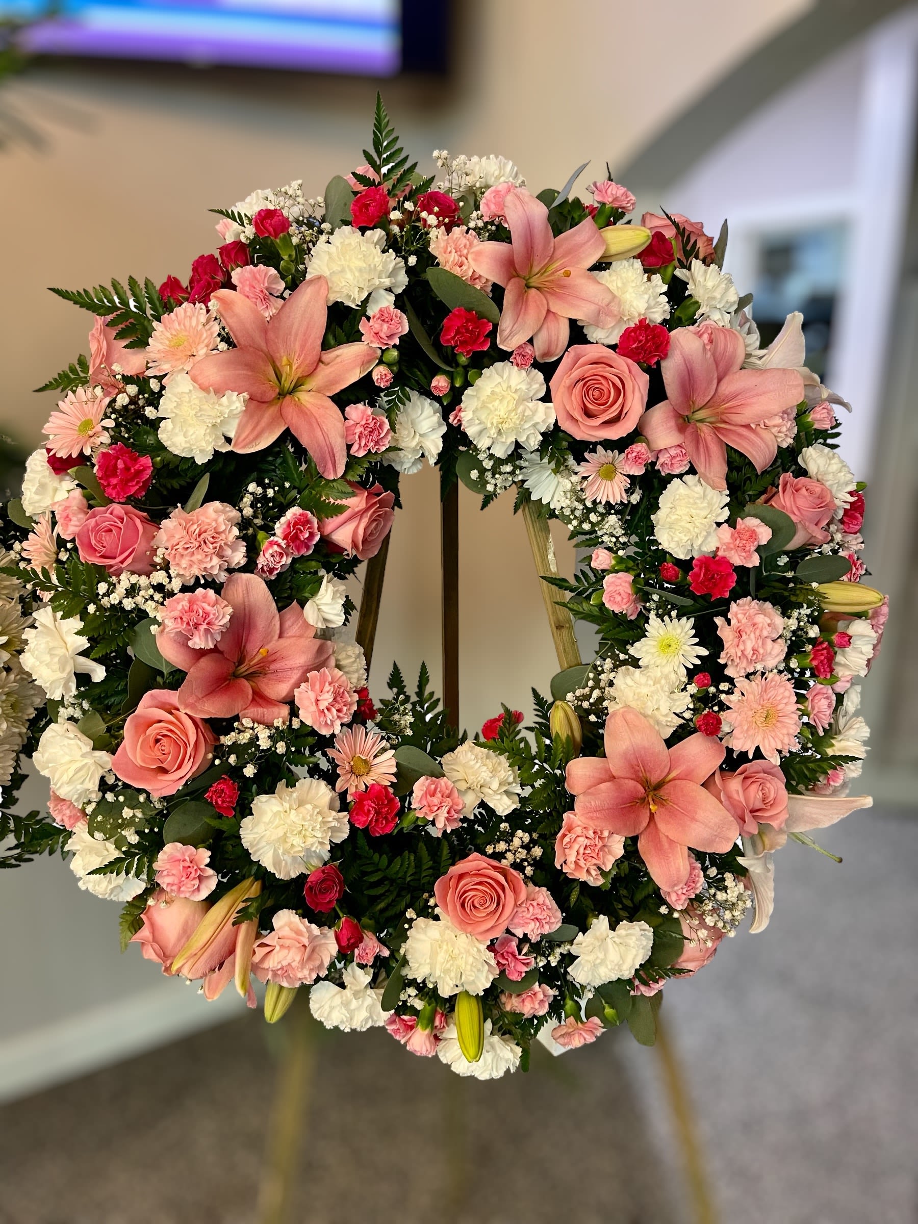 Standing wreath of pink lilies, roses, and mixed white and pink flowers on an easel