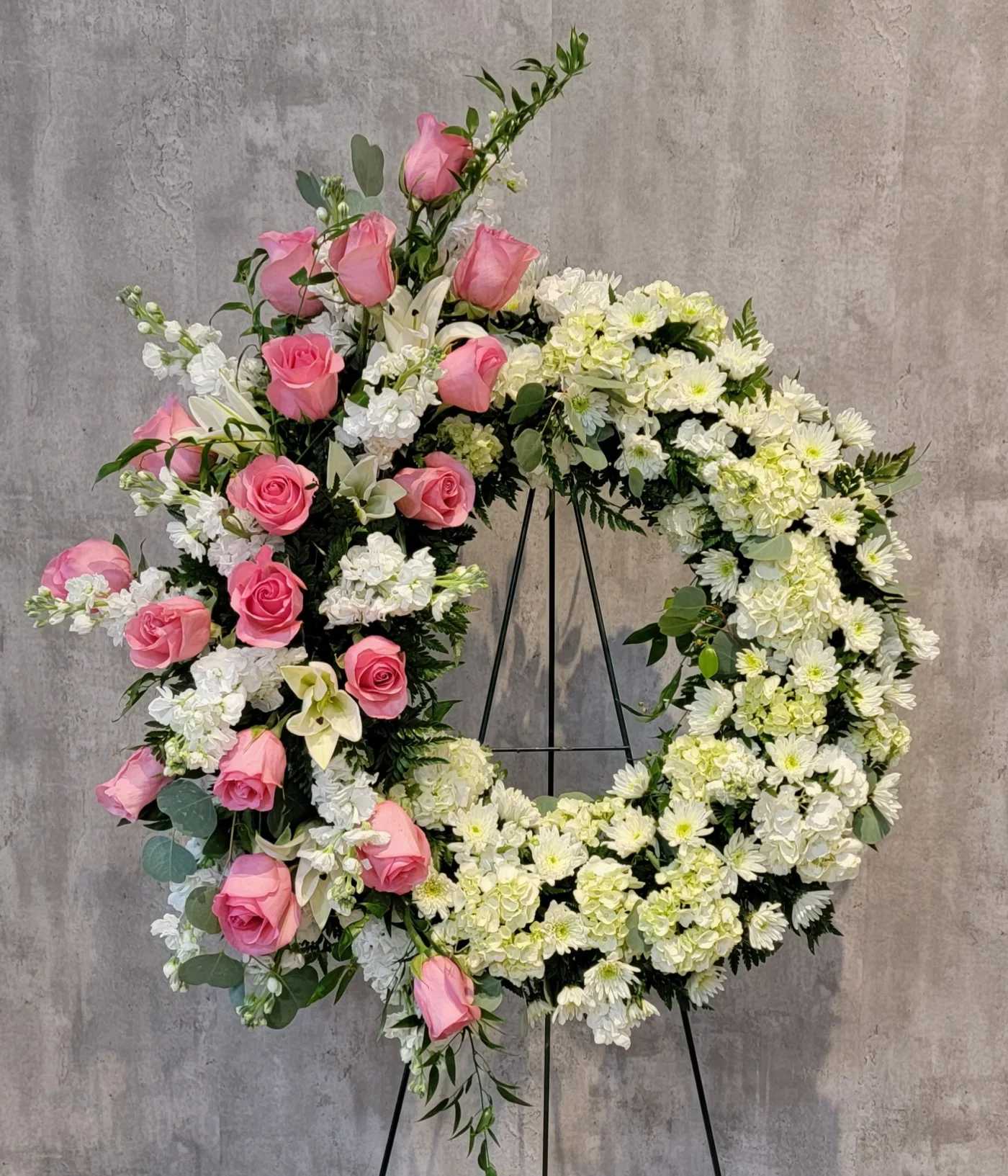 Standing wreath of white flowers with cascading pink roses on a metal easel