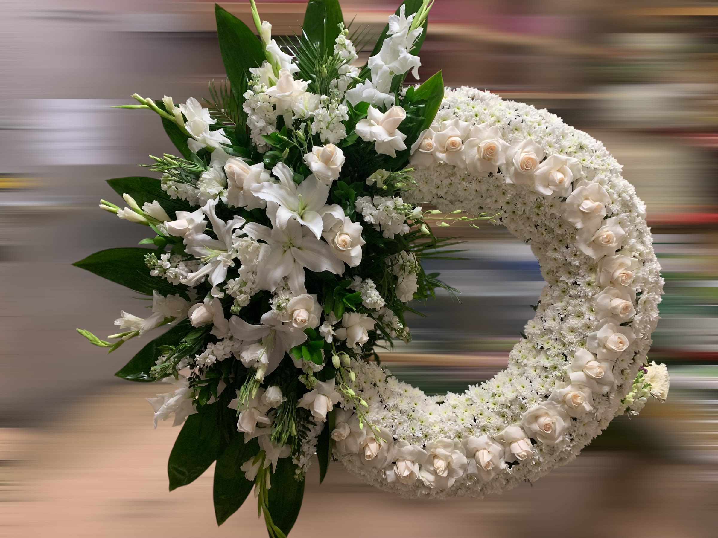 Large white funeral wreath with roses and lilies clustered on one side of the ring