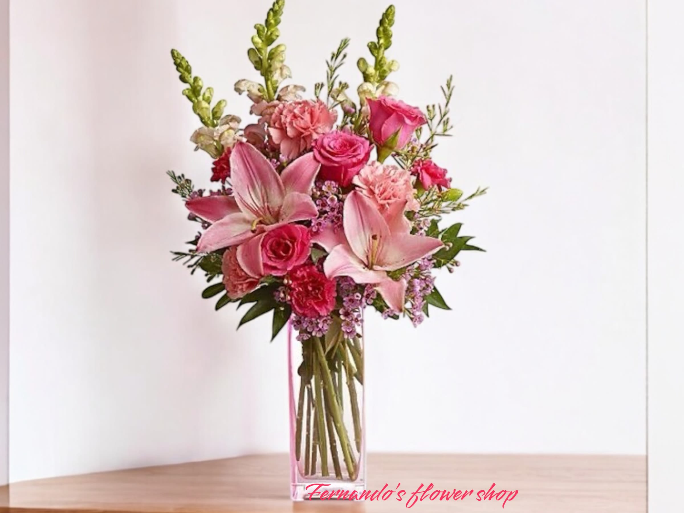 Tall pink arrangement with lilies, roses, and carnations in a clear rectangular glass vase