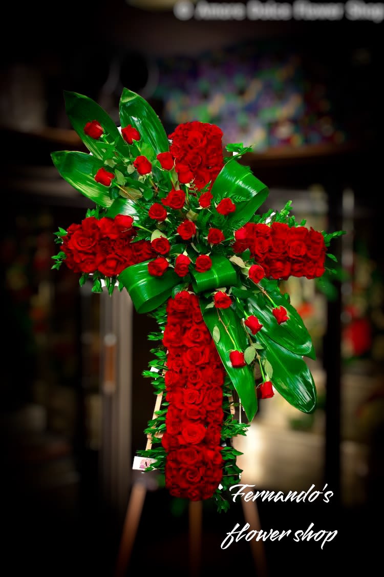 Tall standing cross of red roses with bold green leaves on an easel