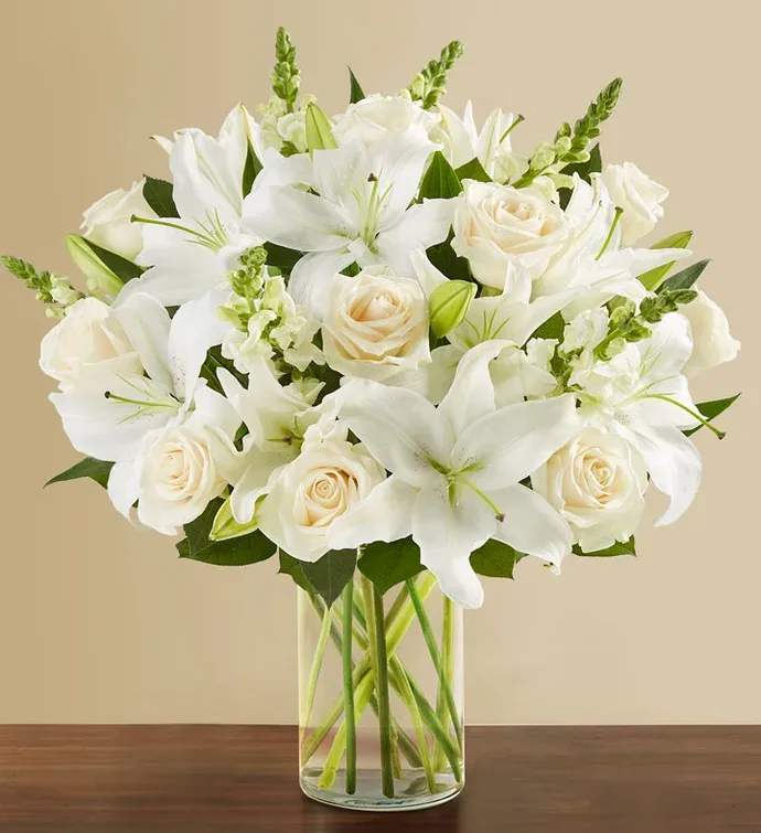 Arrangement of white lilies and cream roses in a clear glass cylinder vase