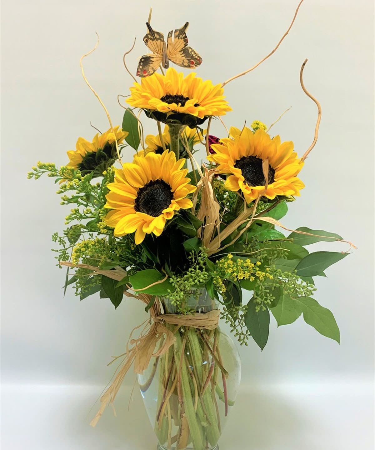 Tall arrangement of yellow sunflowers with rustic accents in a clear glass vase