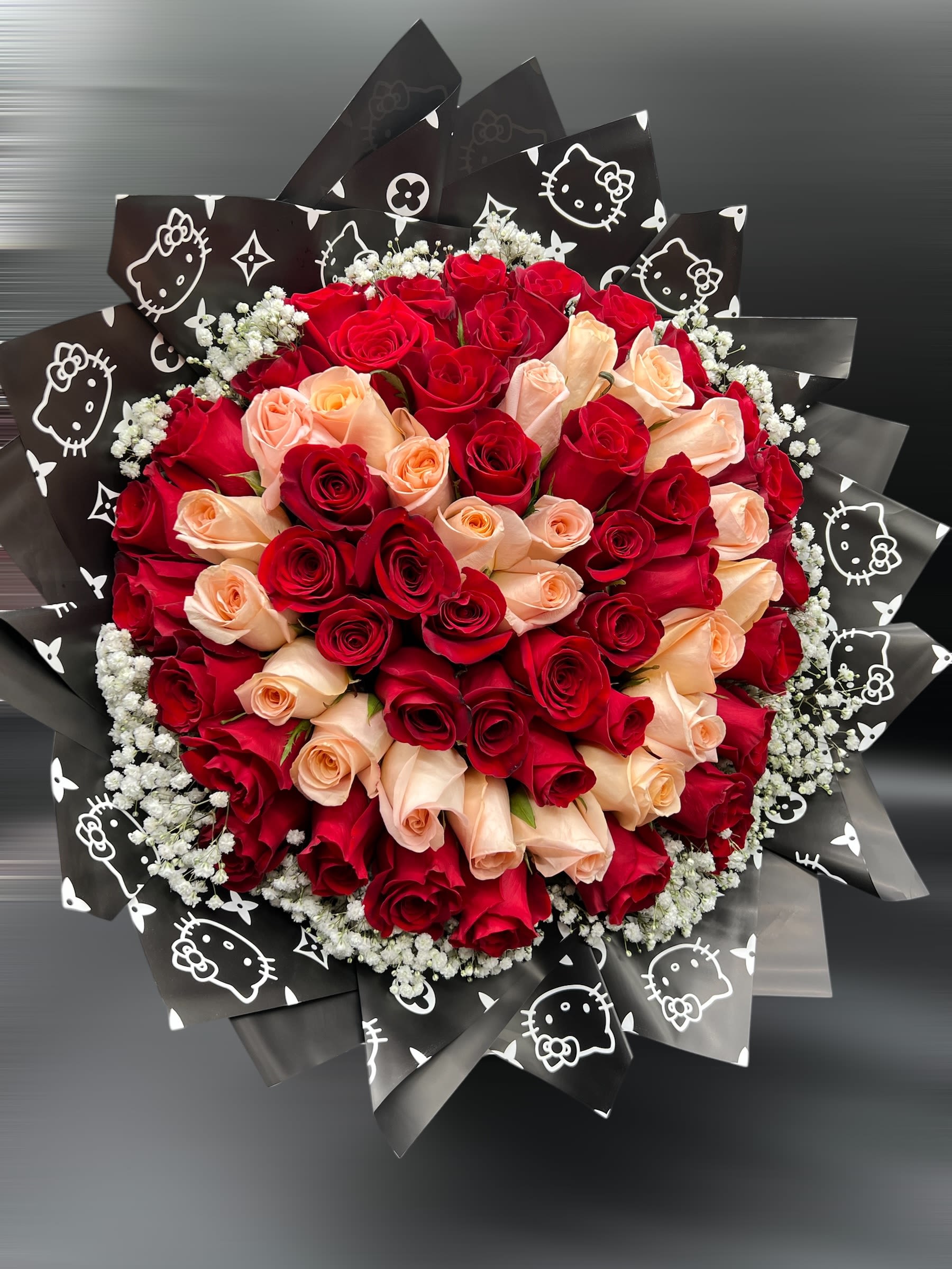 Round bouquet of red and peach roses with white filler wrapped in black printed paper