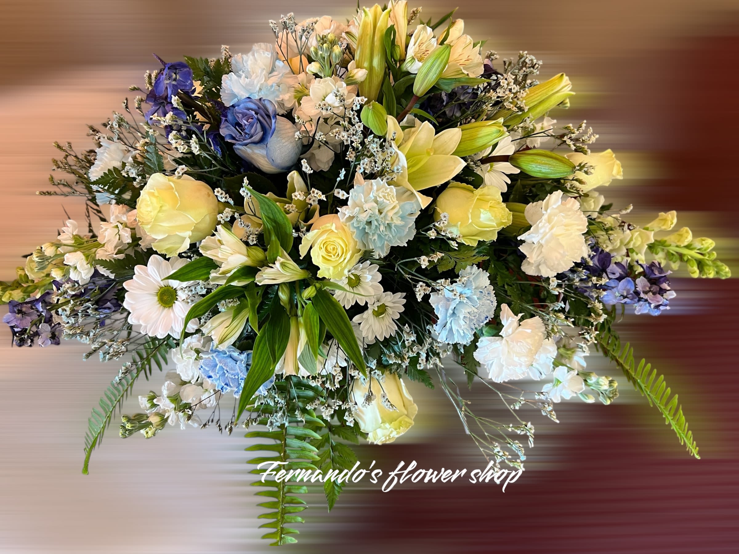 Rounded arrangement of yellow roses, white lilies, daisies and blue flowers in soft pastel tones