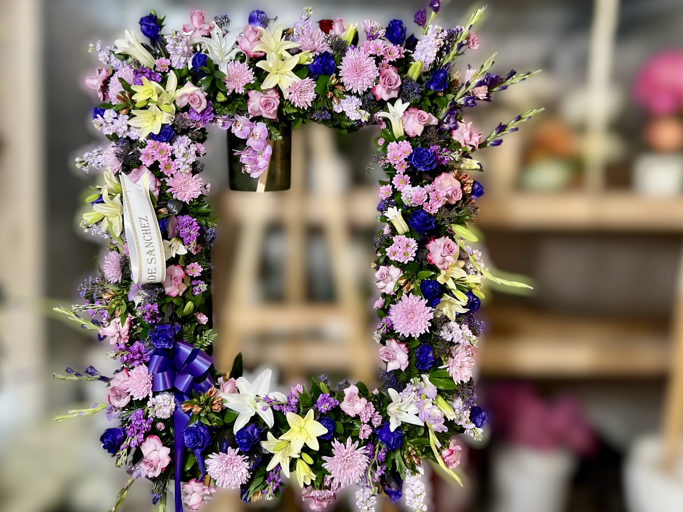 Standing rectangular wreath of pink, purple, yellow, and white flowers with ribbons on an easel