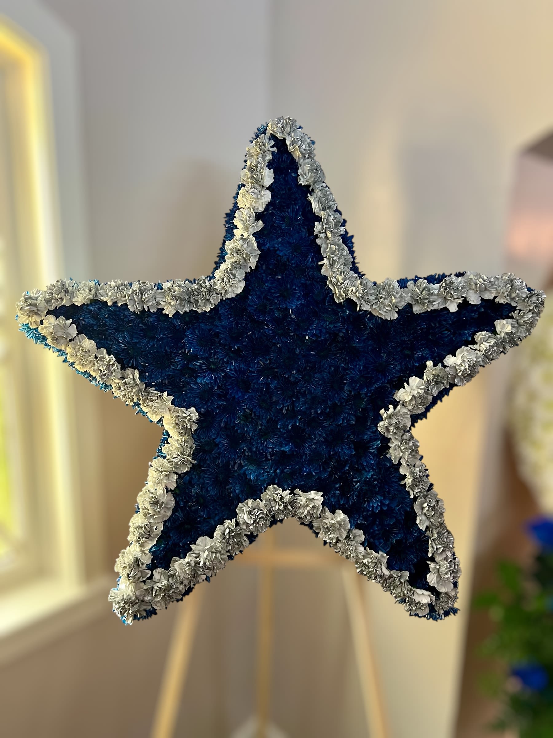 Large blue and white star-shaped standing floral arrangement on a wooden easel