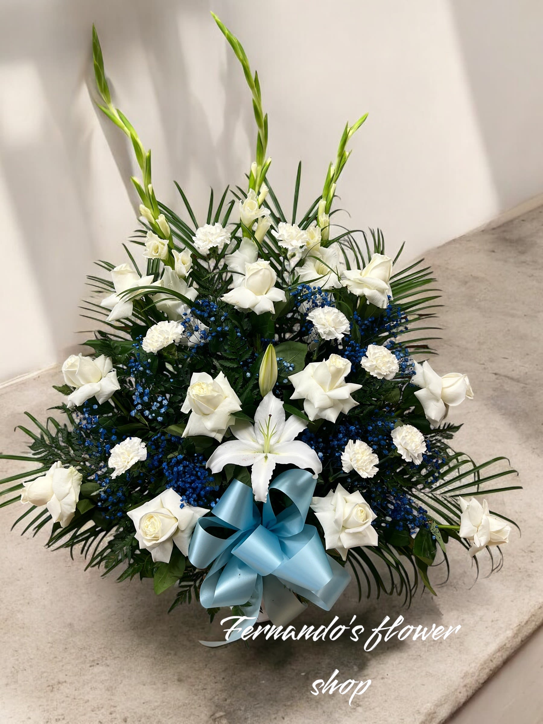 Fan-shaped white roses, carnations, and lilies with blue accents and a light blue bow.